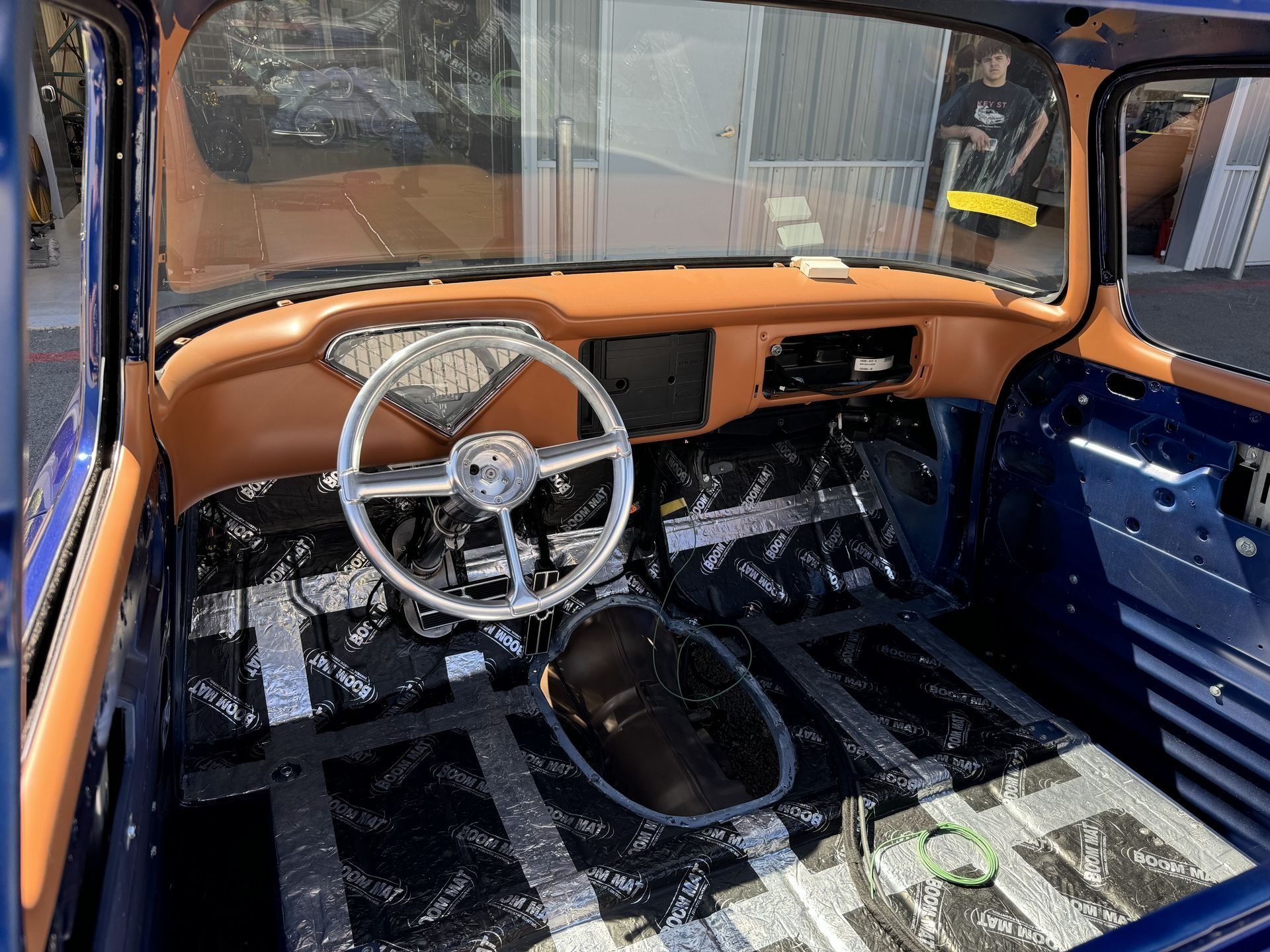 Vintage car interior with blue panels, tan dashboard, and white steering wheel, stripped floor visible