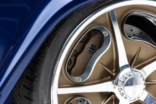 Close-up of a blue car’s gold alloy wheel and tire with chrome detailing