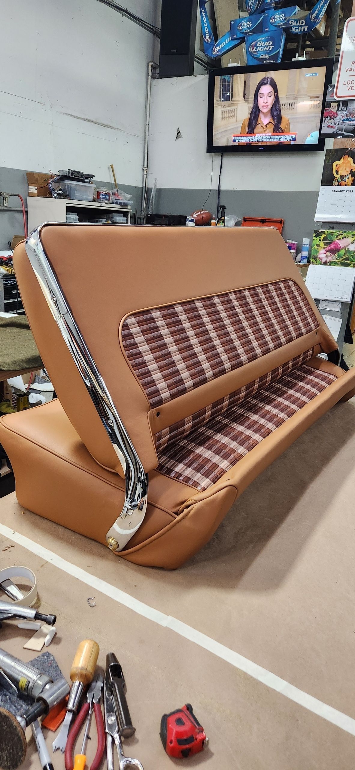 Brown fold-out sofa bed in a cluttered living room, with a TV mounted on the wall above it.