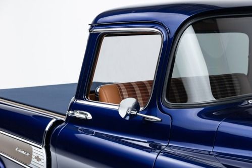 Close-up of a glossy blue vintage pickup truck cab and bed with a chrome side mirror.
