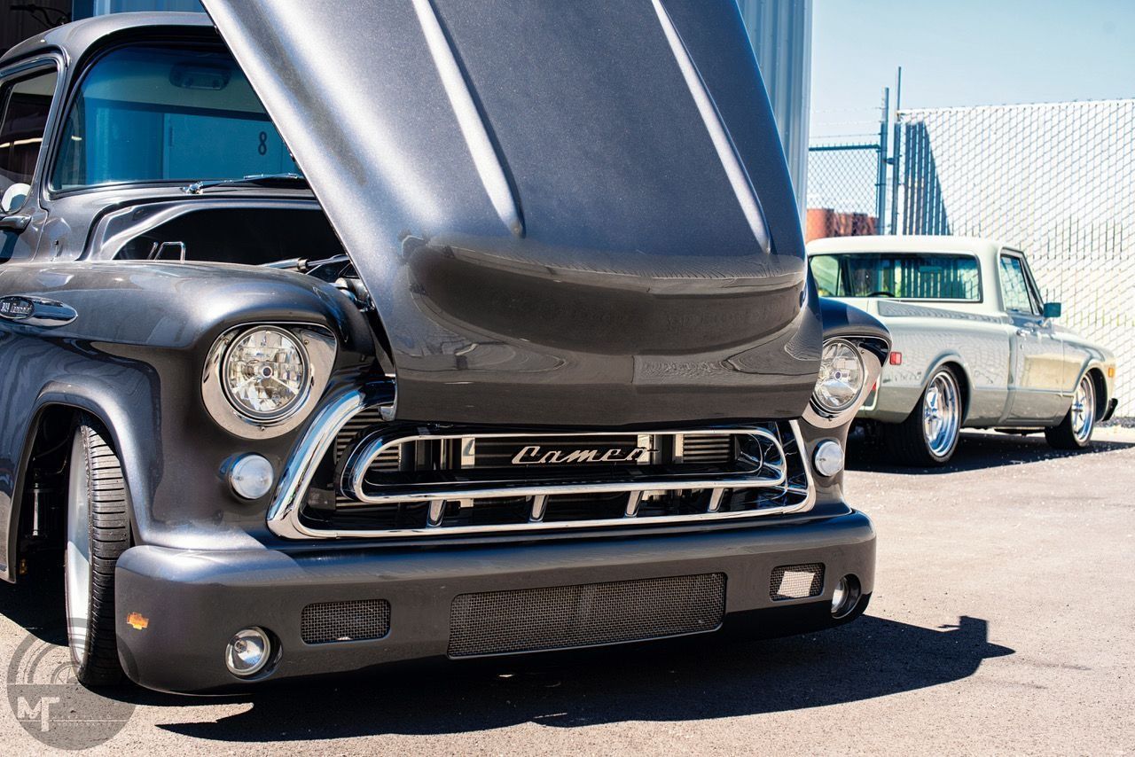 Classic black hot rod with hood raised at an outdoor car show, with vintage cars in the background