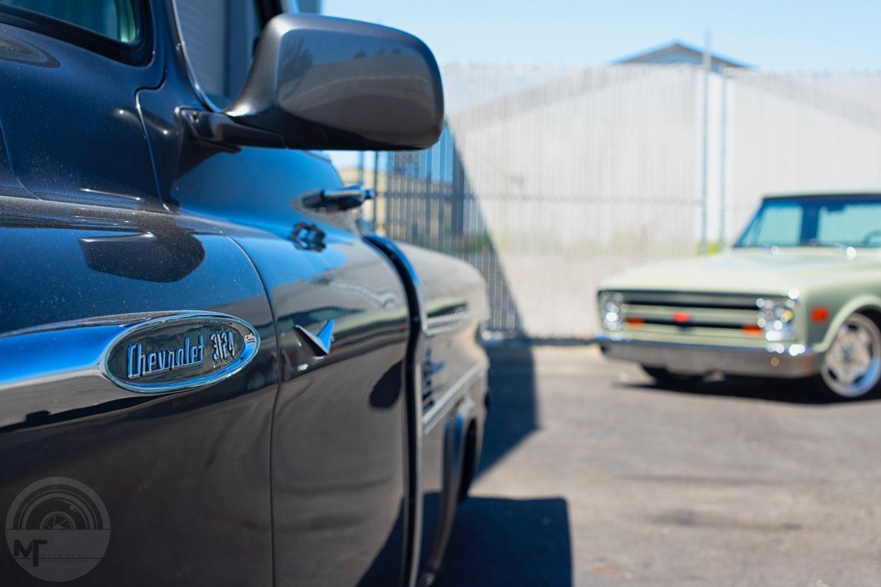 Black classic car in foreground with blue car and cream convertible in background on a sunny lot