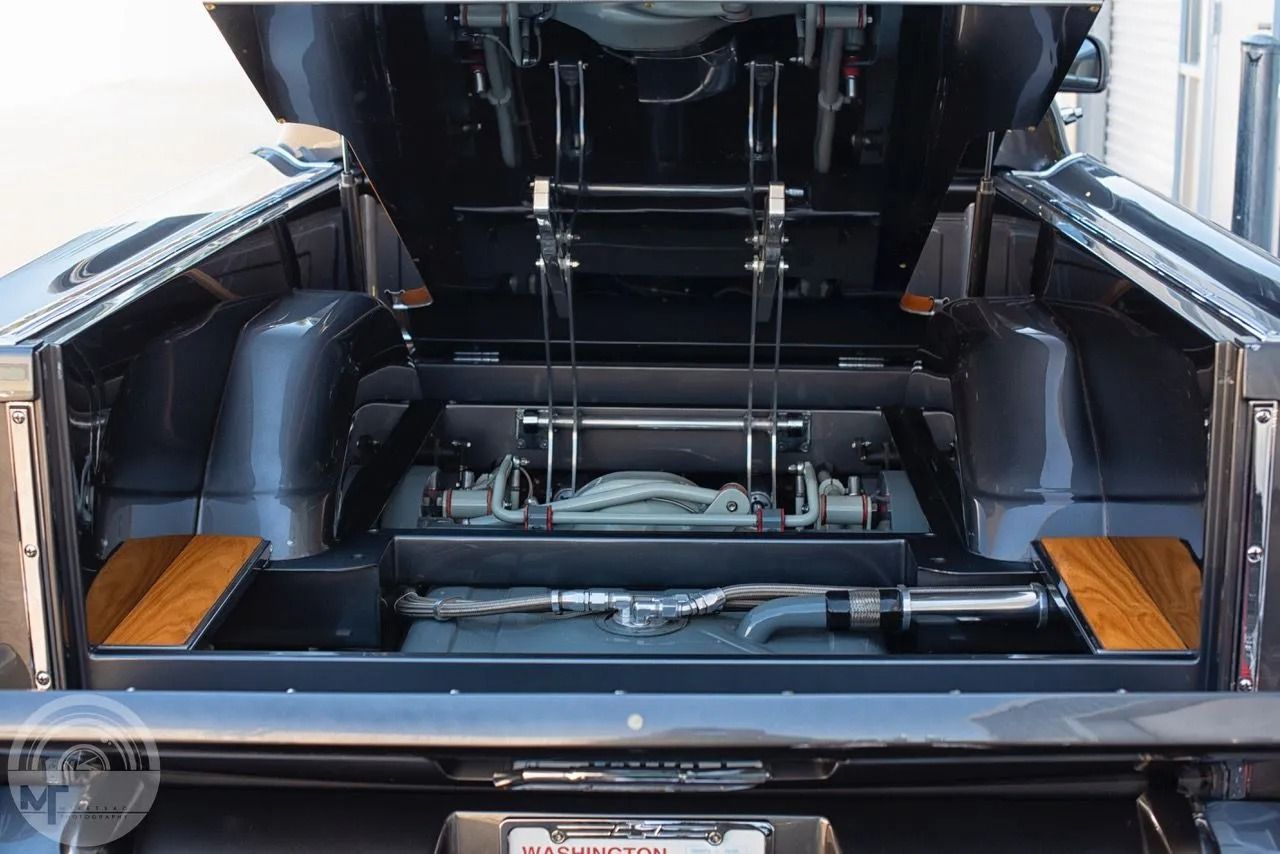 Rear engine compartment of a black sports car with the hatch open, showing the engine bay and mechanical components