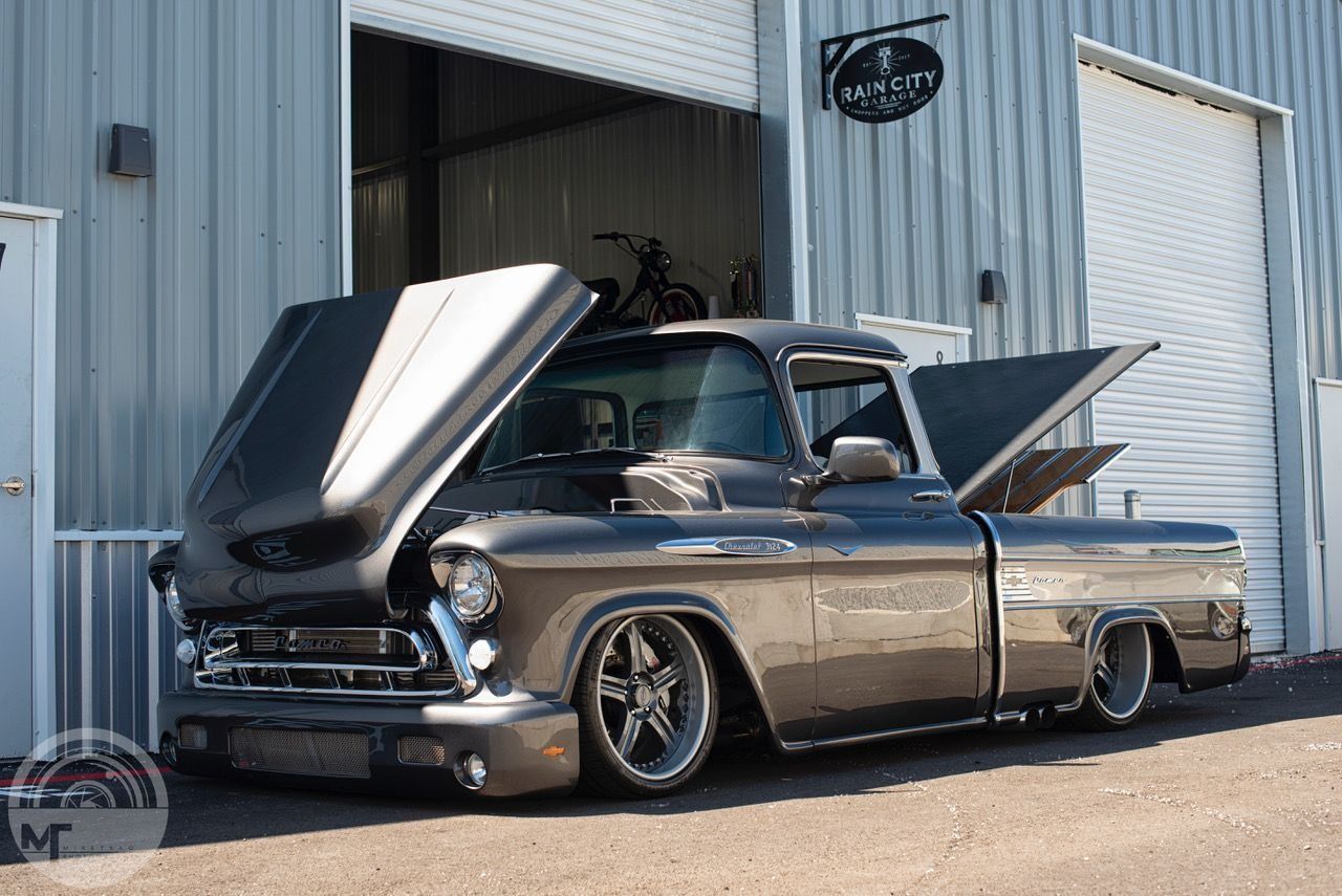 Lowrider classic car with open hood parked outside an industrial building