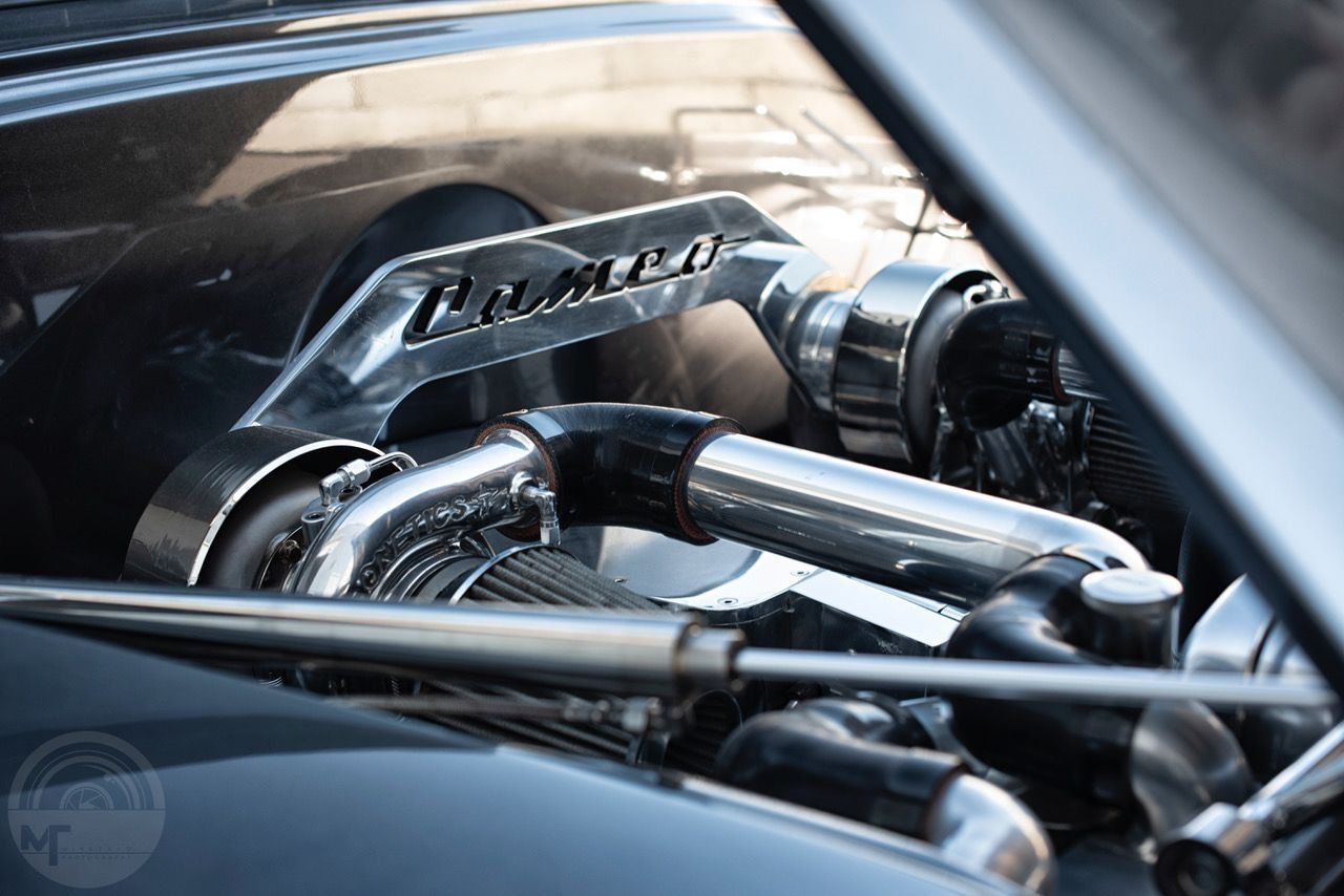 Chrome engine components inside a car, with polished intake pipes and a “Corsa” badge.