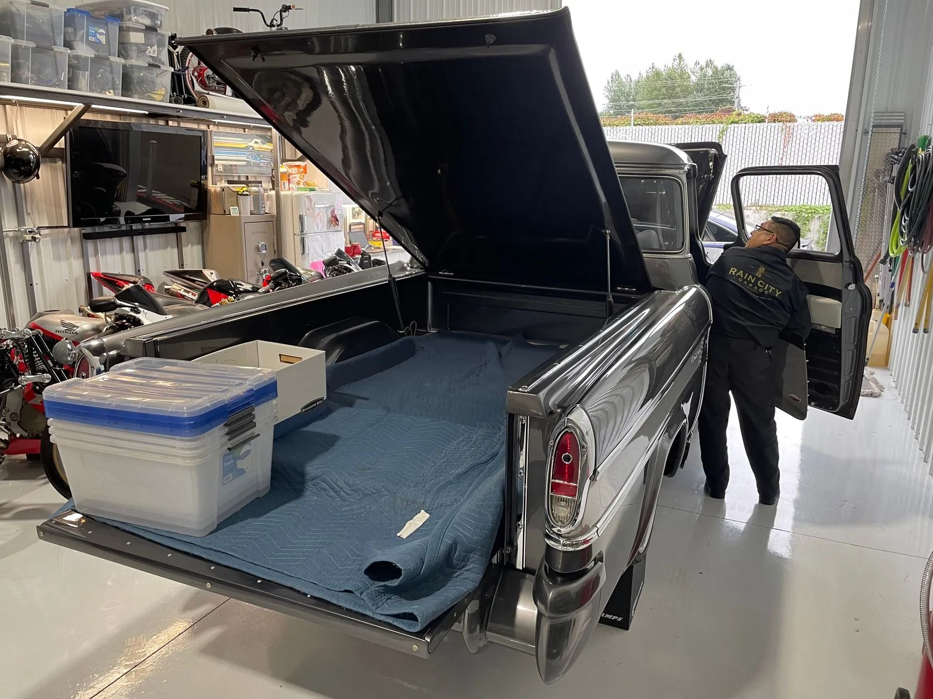 Black pickup truck with open canopy and tailgate, cargo area exposed in a garage-like workshop.