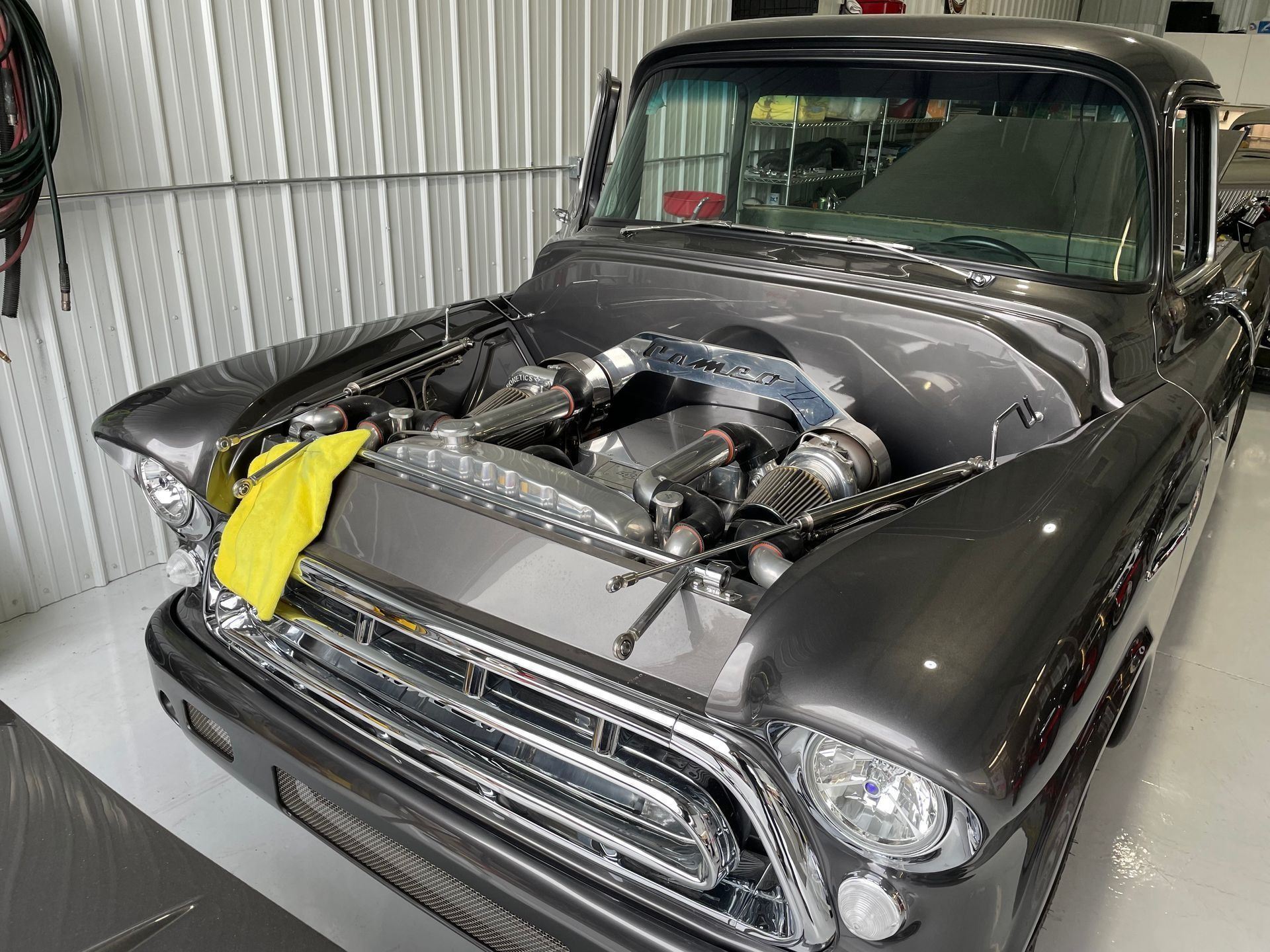Classic black car in a garage with hood open, showing a modified engine and yellow cloth on the front.
