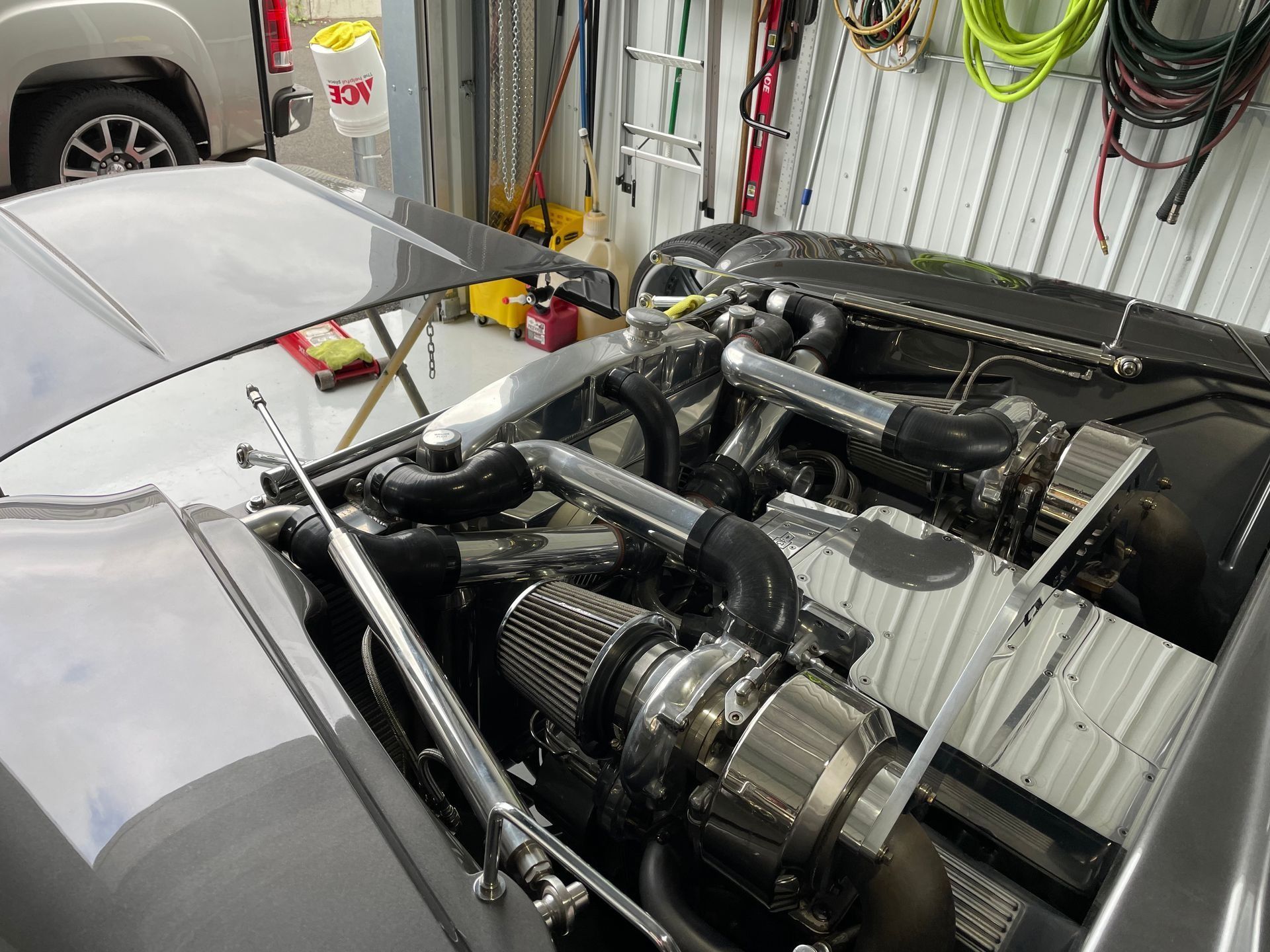 Rear view of a silver sports car with an open engine bay showing exposed engine components in a garage