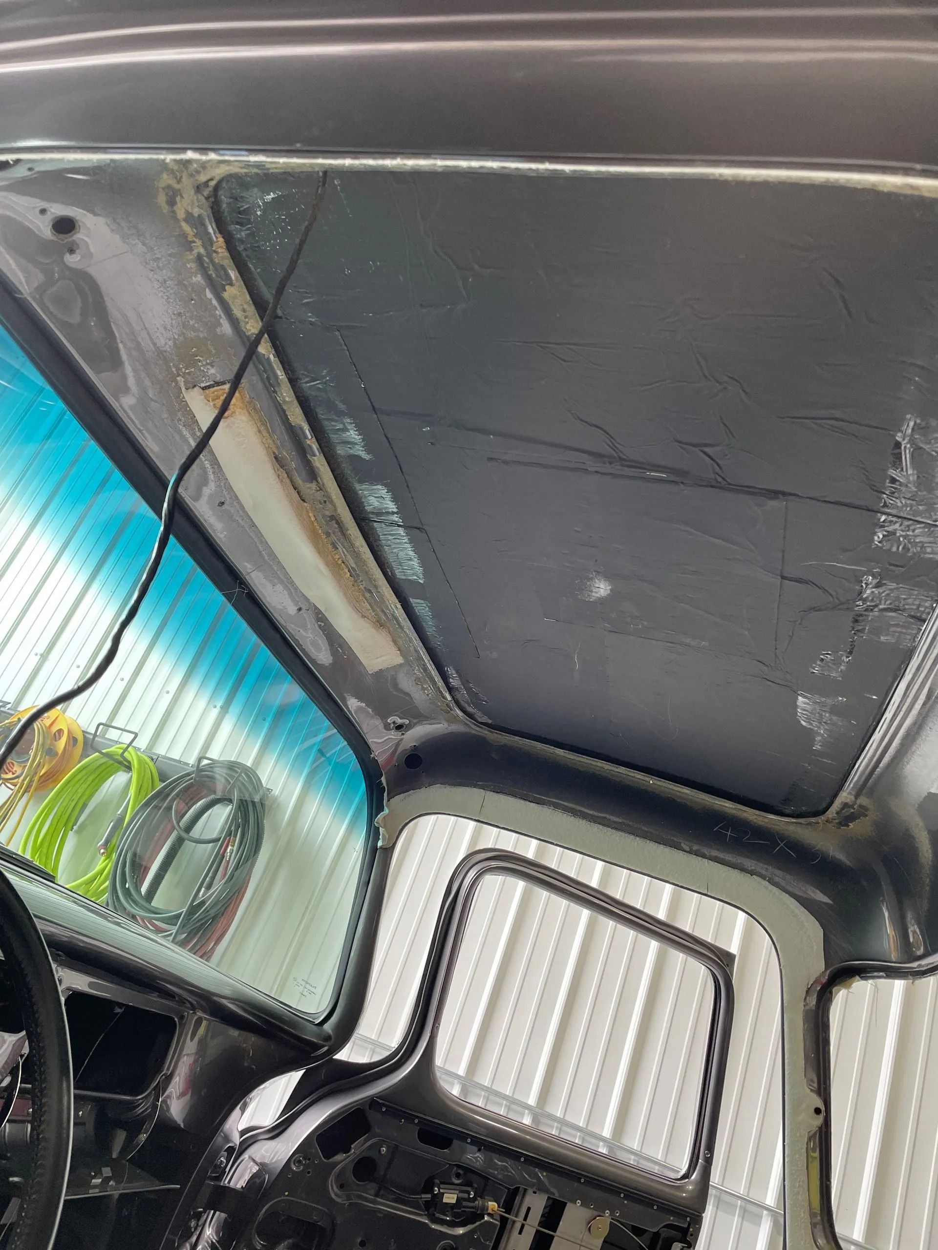 Interior of a vehicle with a damaged, sagging black roof liner and visible condensation on the window.