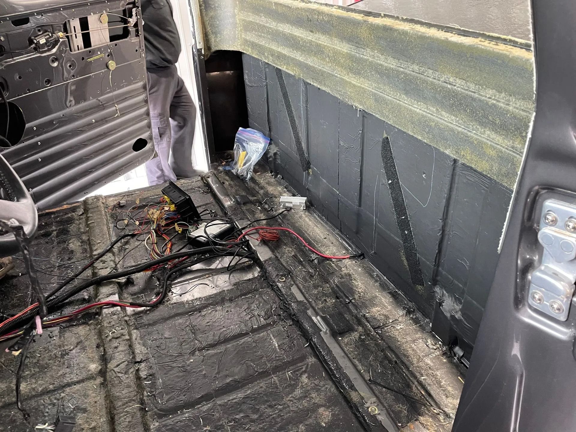 Inside a vehicle cargo area, exposed wiring and loose debris lie on a dirty black floor