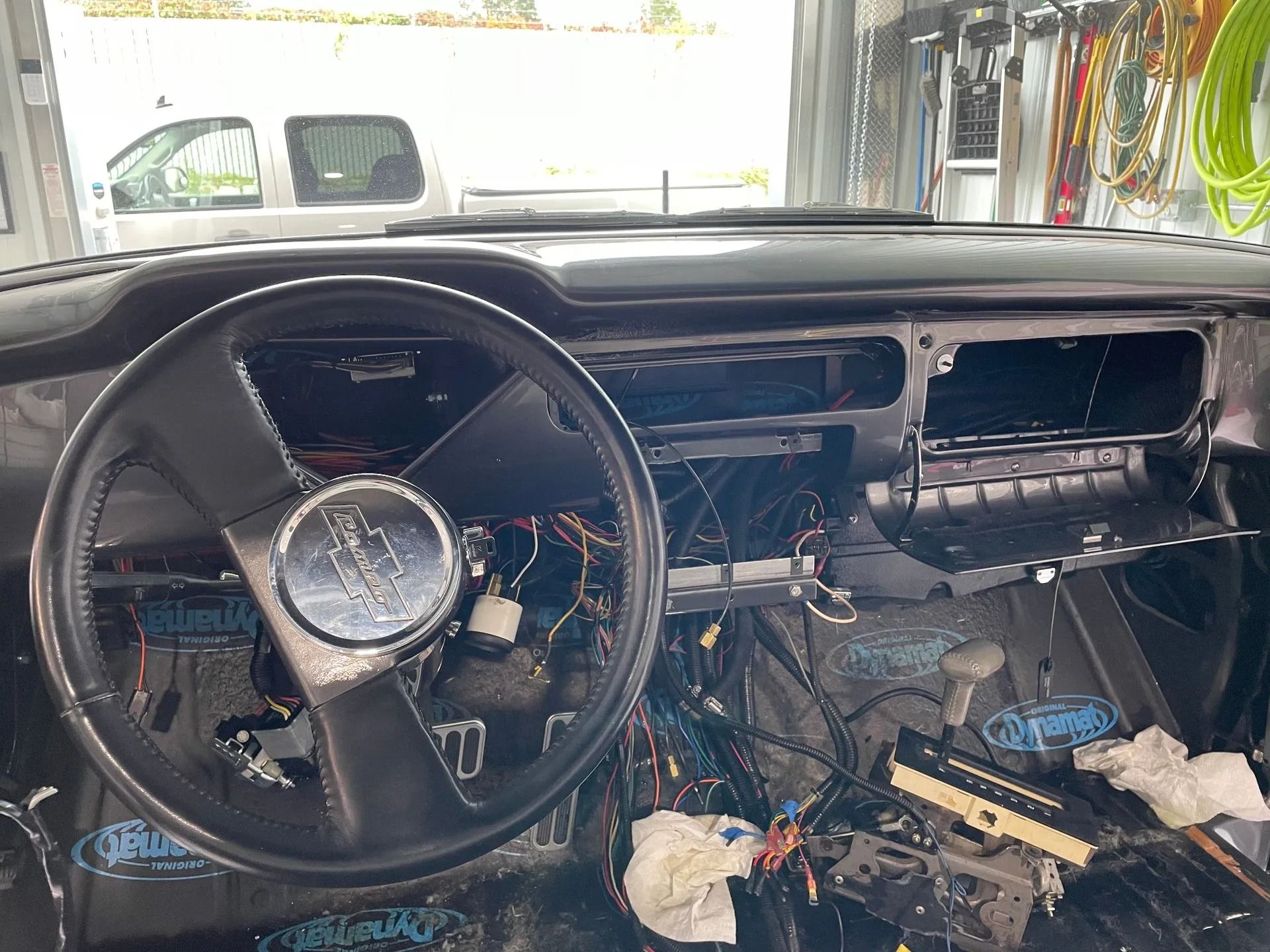 Stripped car dashboard and exposed wiring inside a vehicle interior, with a steering wheel in front