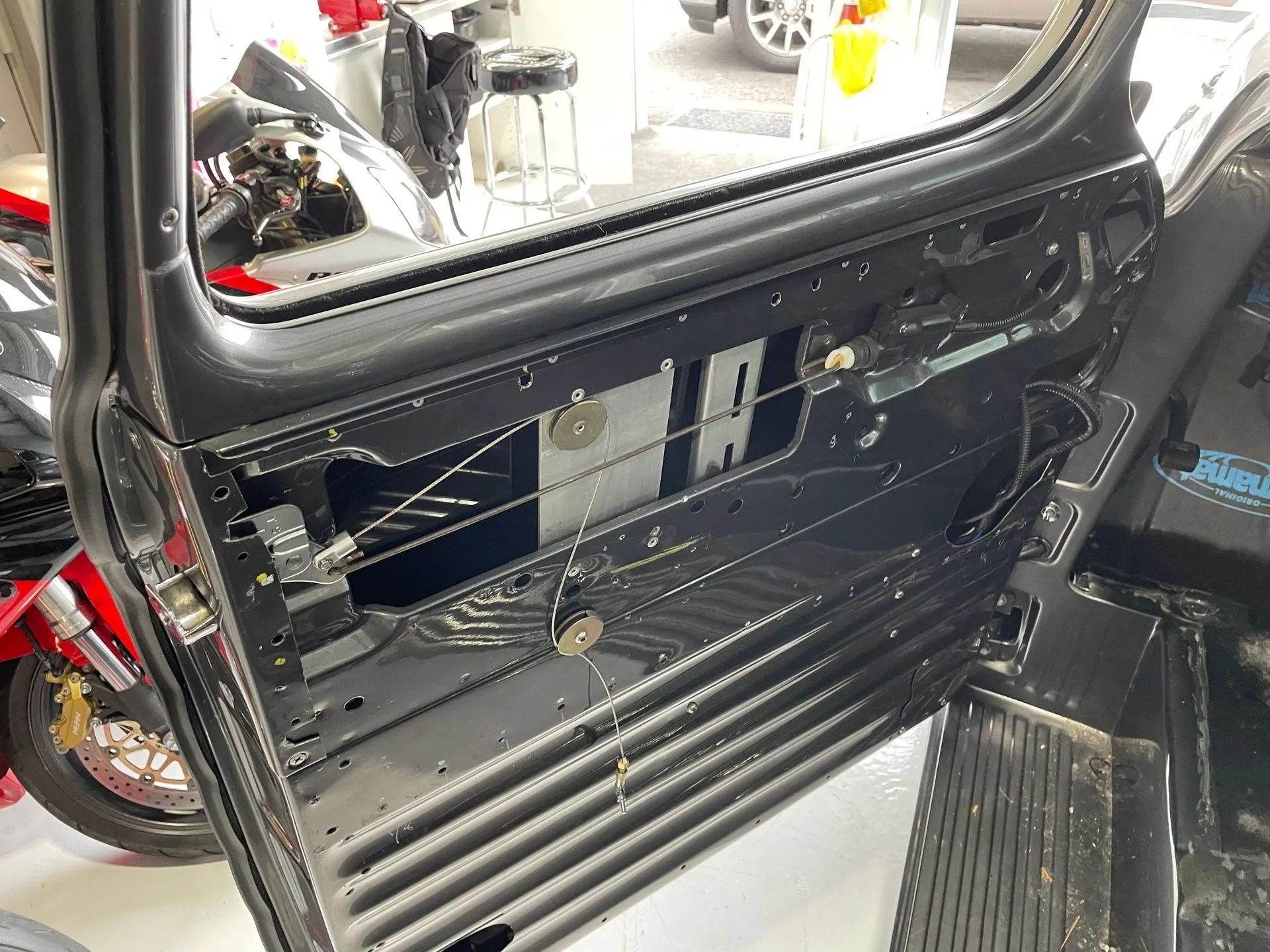 Open car door with exposed interior panels and wiring, showing a black vehicle door frame and seat.