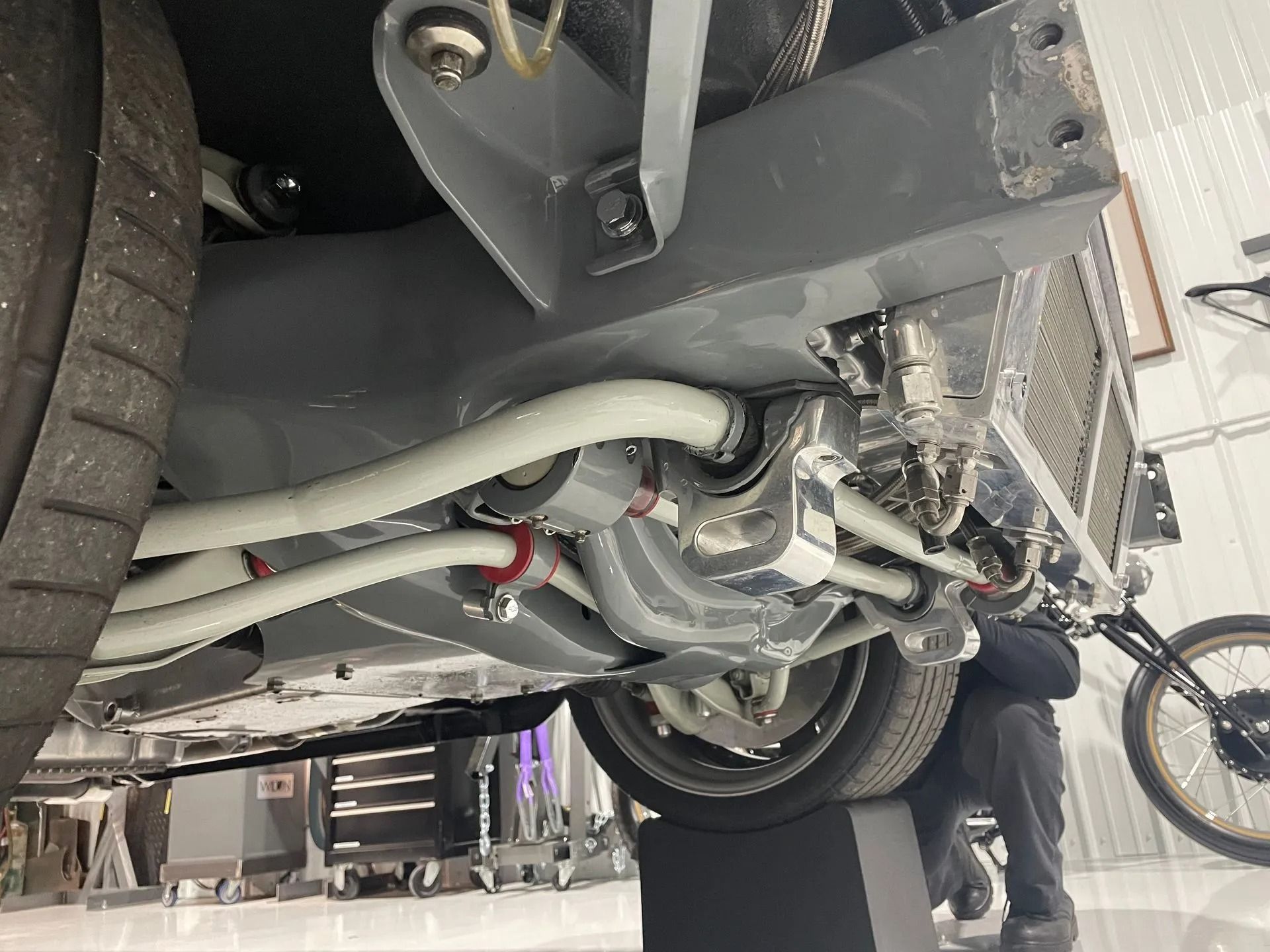 Undercarriage of a car with exhaust and suspension visible, lifted in a workshop with a person nearby