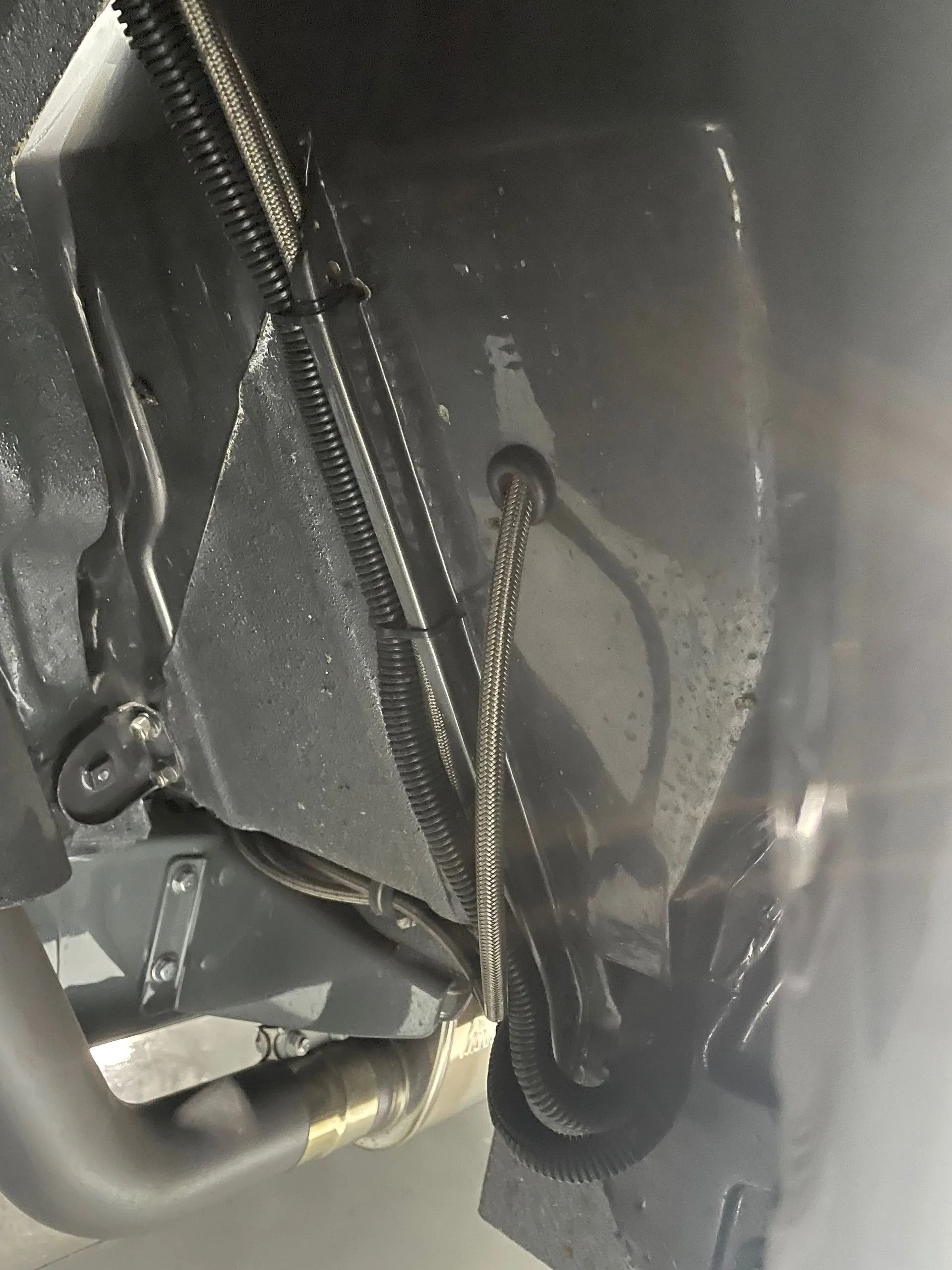 Close-up of black machinery with a chain, cable, and metal tubing inside a dark compartment