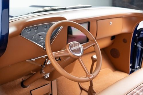 Vintage car interior with tan leather seats, wood dashboard, and steering wheel.