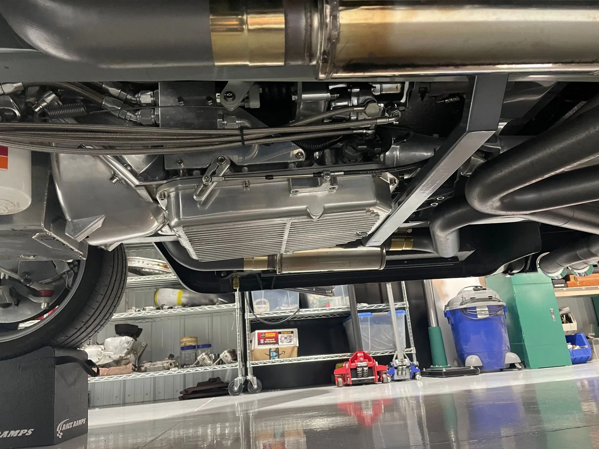 Underside of a vehicle on a lift in a garage, with tools and bins in the background