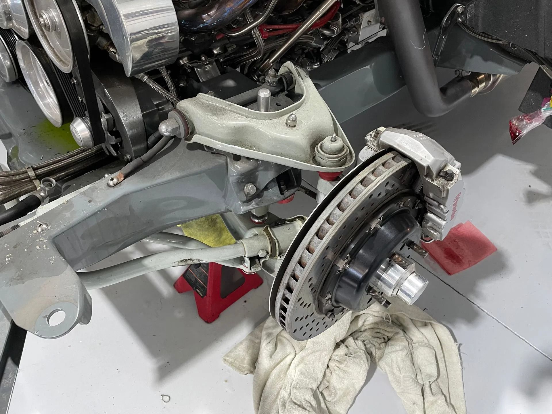 Brake disc and suspension assembly on a car, with a gloved hand working underneath on a lift.