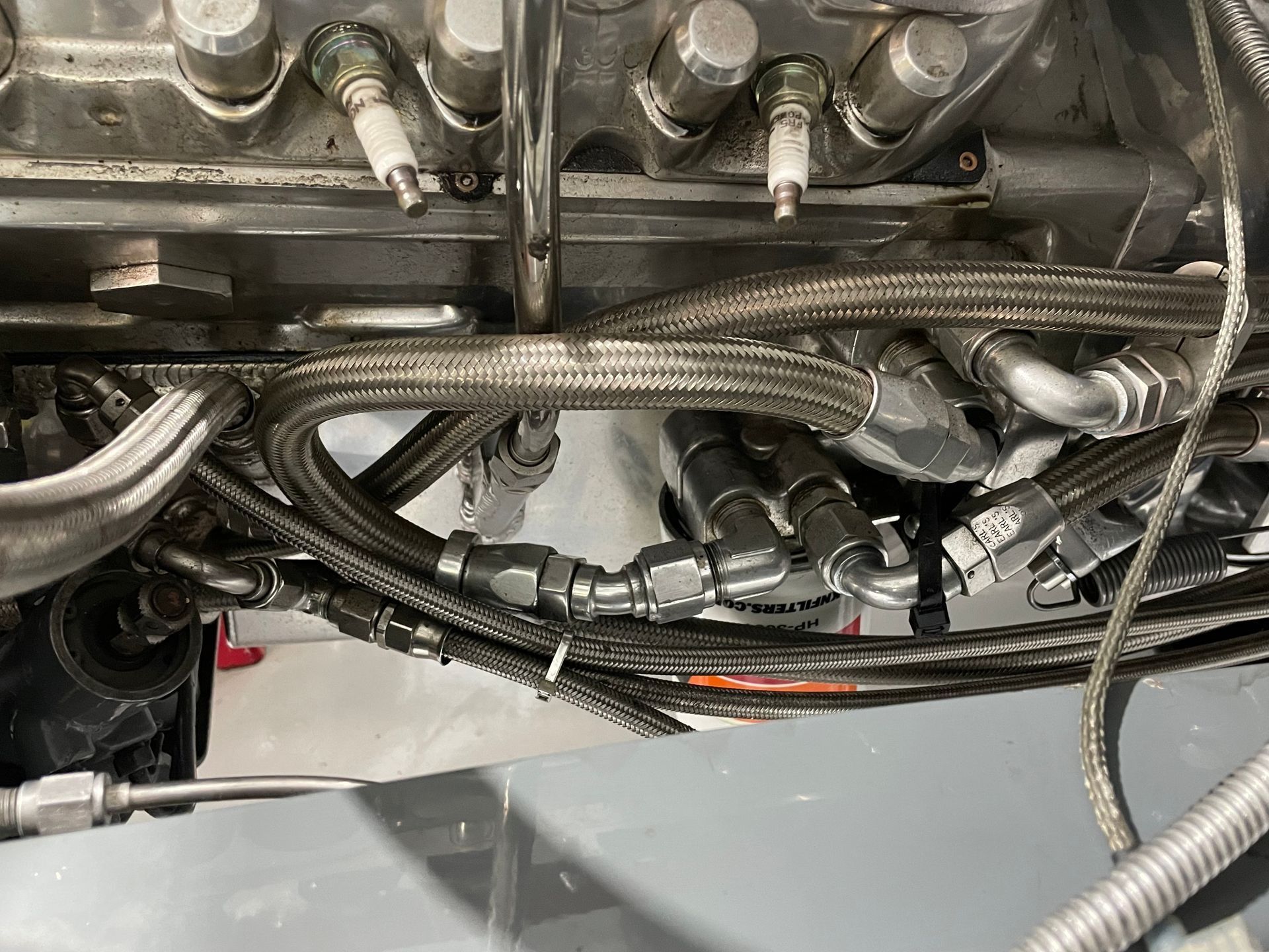 Close-up of an engine compartment with braided hoses, wiring, and metal fittings underneath machinery.