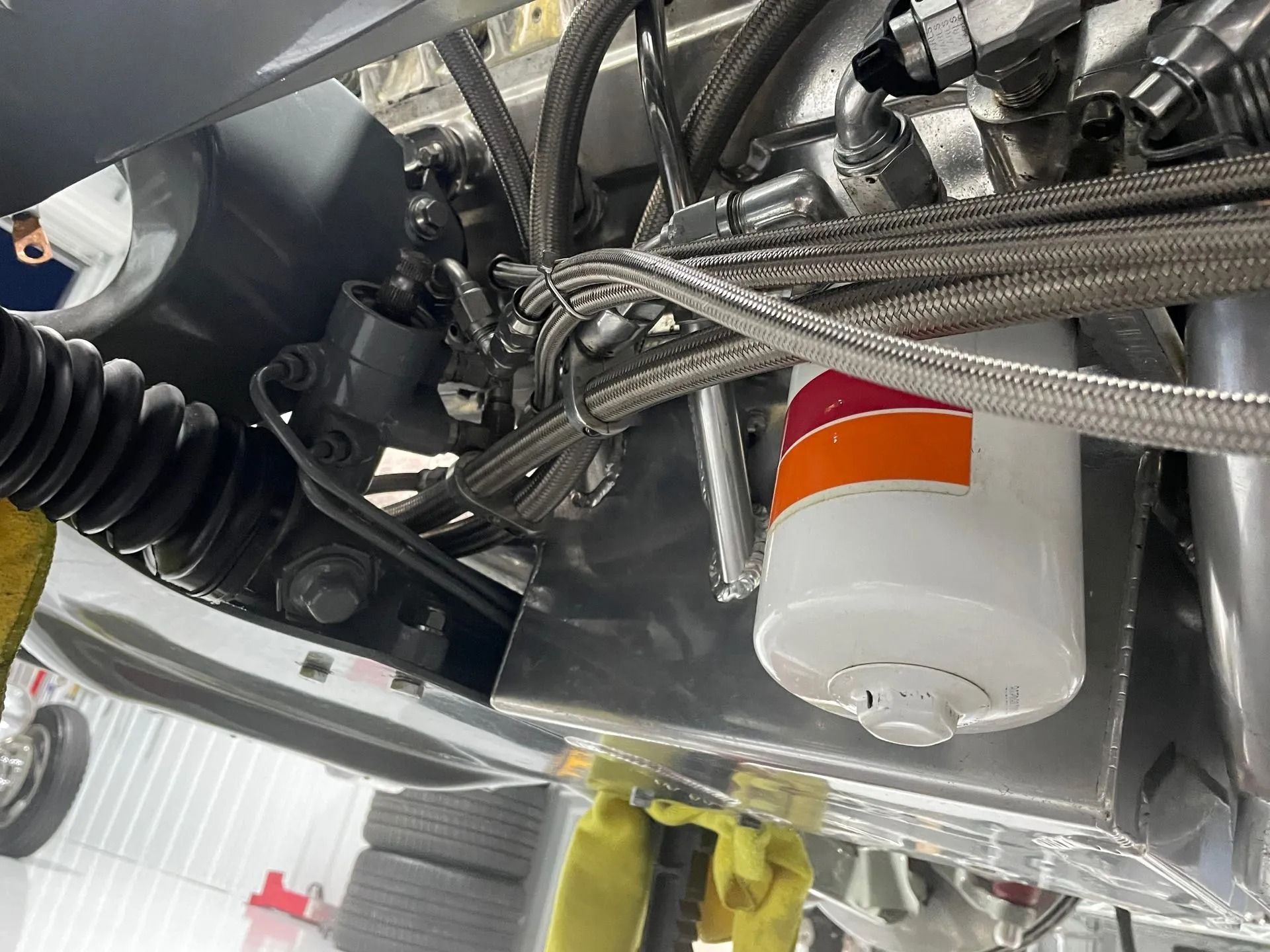 Close-up of machinery with braided hoses, metal fittings, and a white cylindrical filter with an orange label.