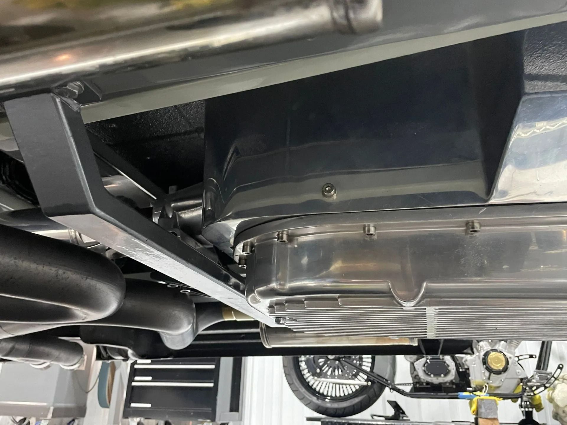 Undercarriage of a vehicle with black frame, exhaust pipes, and a metal fuel tank.