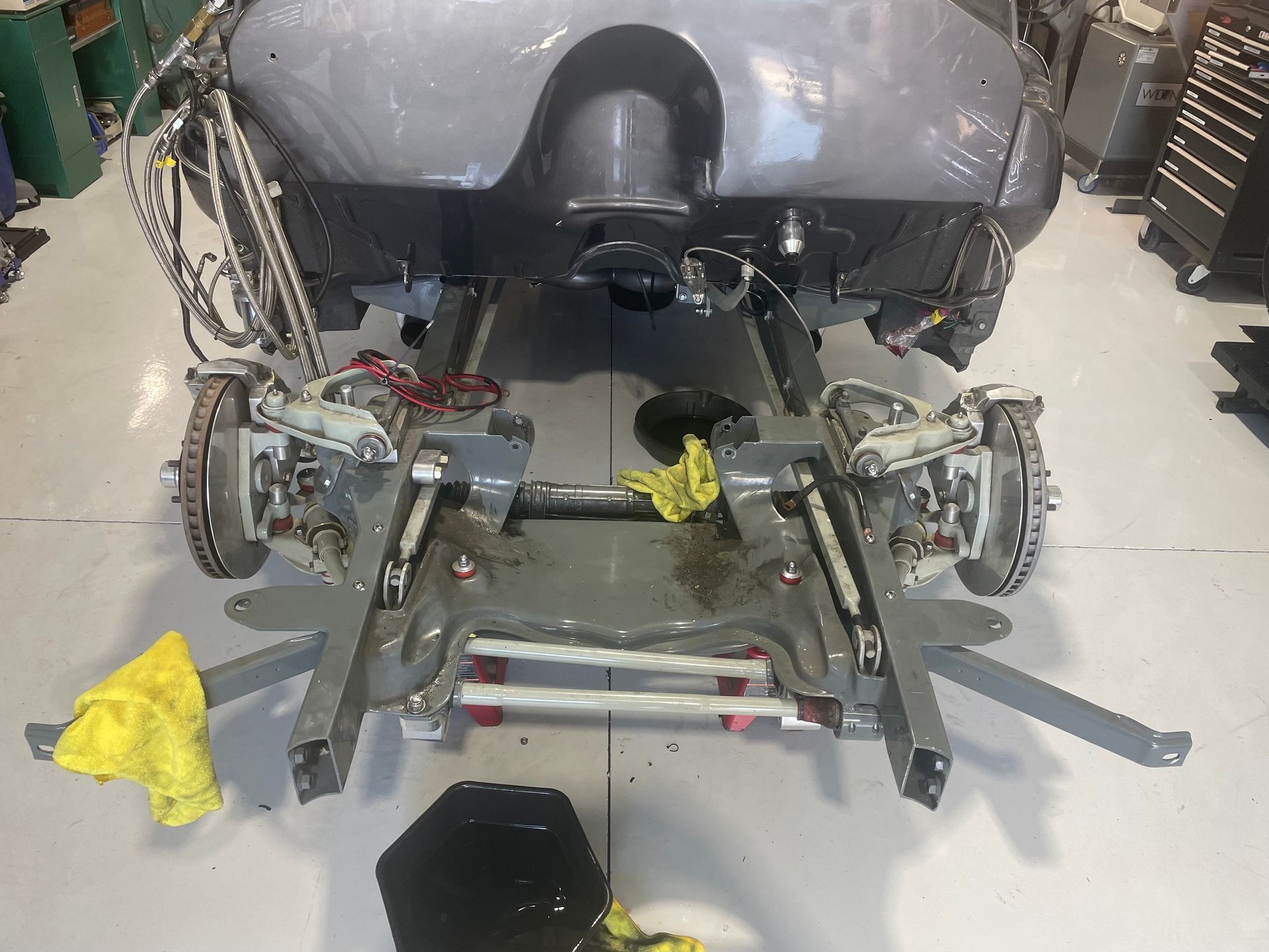 Car undercarriage on a repair lift in a garage, with exposed suspension and tools nearby