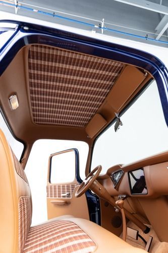 Vintage car interior with tan upholstery and woven ceiling panel, viewed from the back seat.