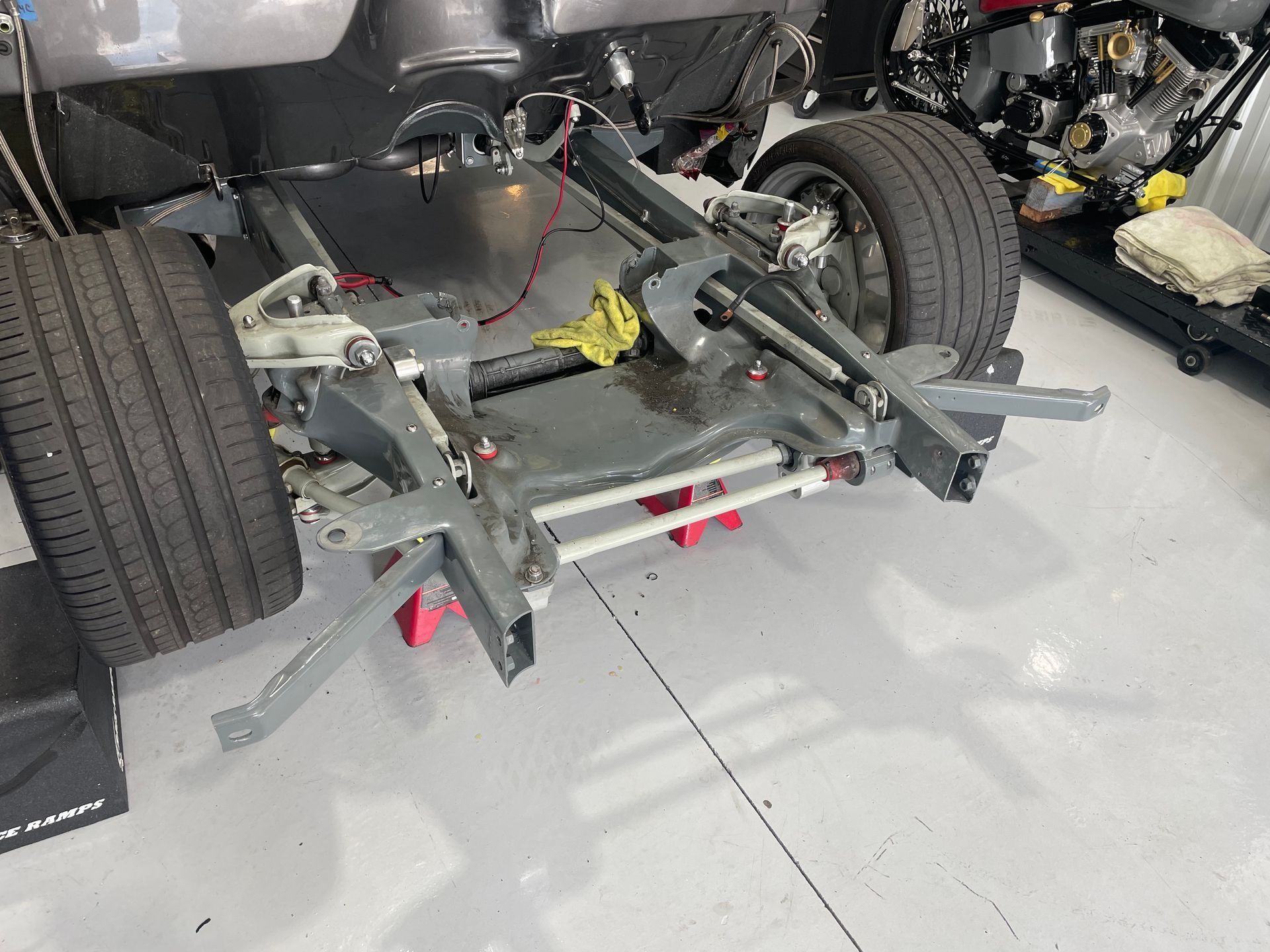 Rear view of a car chassis with exposed suspension, wheels, and metal frame in a garage workshop