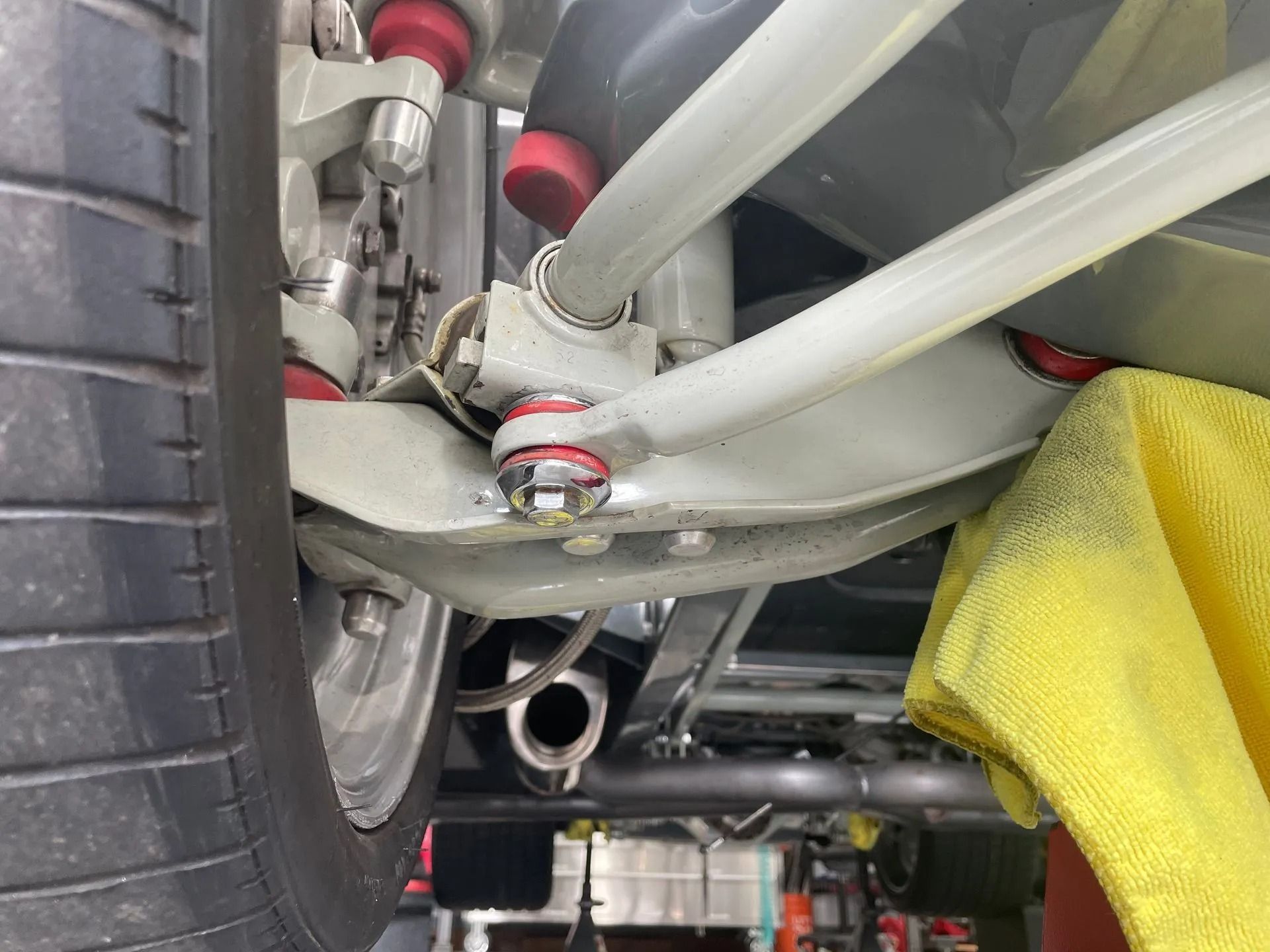 Low-angle view of a car’s rear suspension and wheel, with white control arms and yellow shop cloth nearby