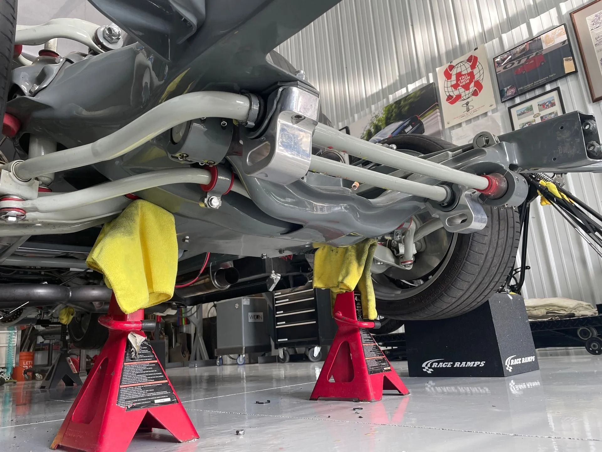 Red sports car raised on jack stands in a garage, with tools and protective padding underneath.