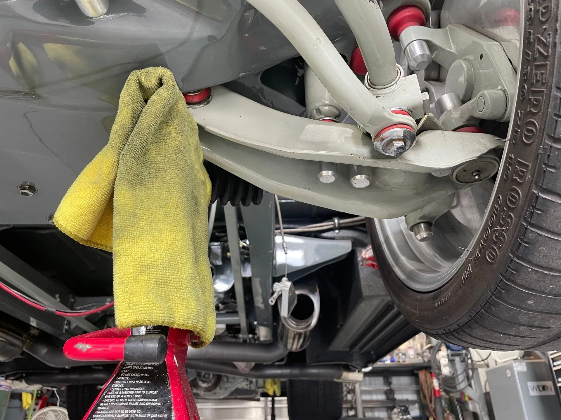 Undercarriage of a car on a lift, with a yellow towel draped over a tool and a wheel visible.