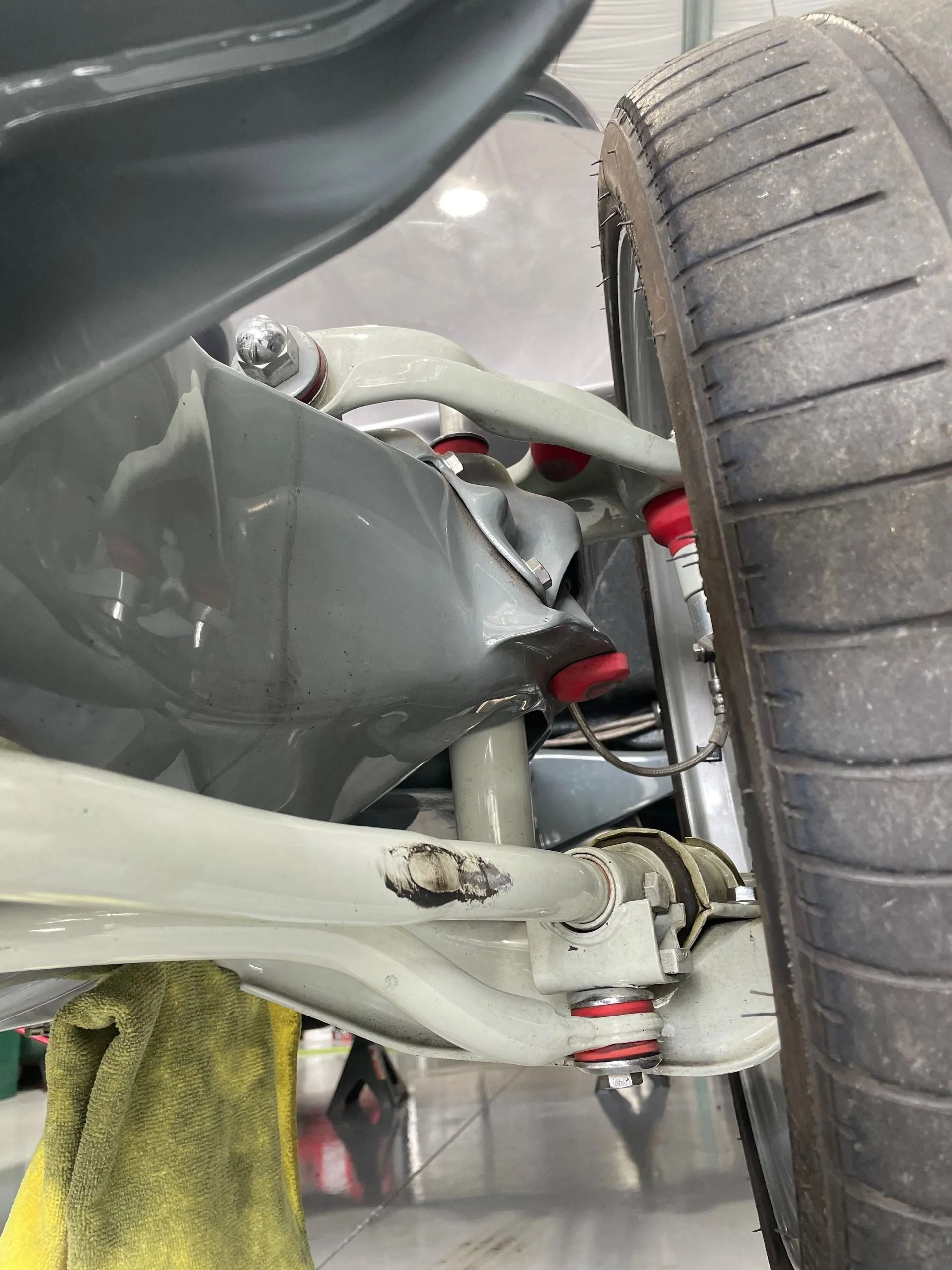Close-up of a car’s rear suspension and wheel, showing gray control arms, red coilover spring, and tire.