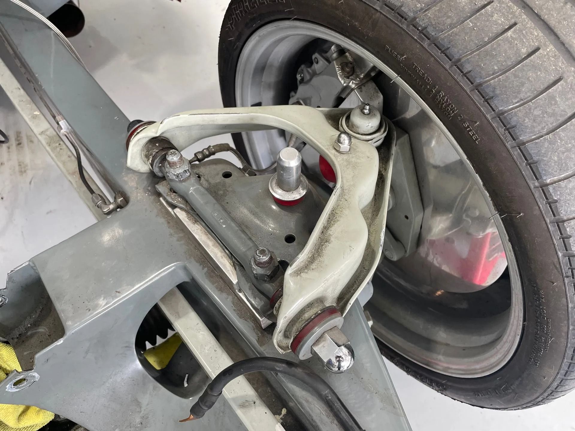 Close-up of a car’s front suspension and wheel assembly with metal control arms and tire.