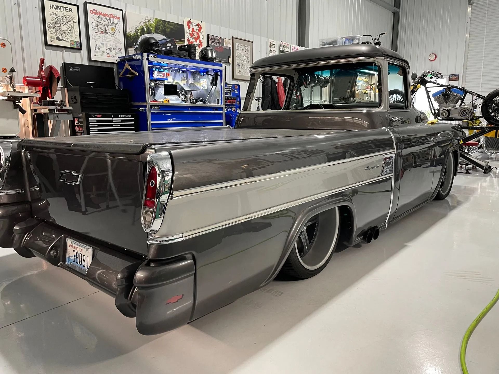 Low-slung black and silver vintage pickup truck in a garage, rear three-quarter view