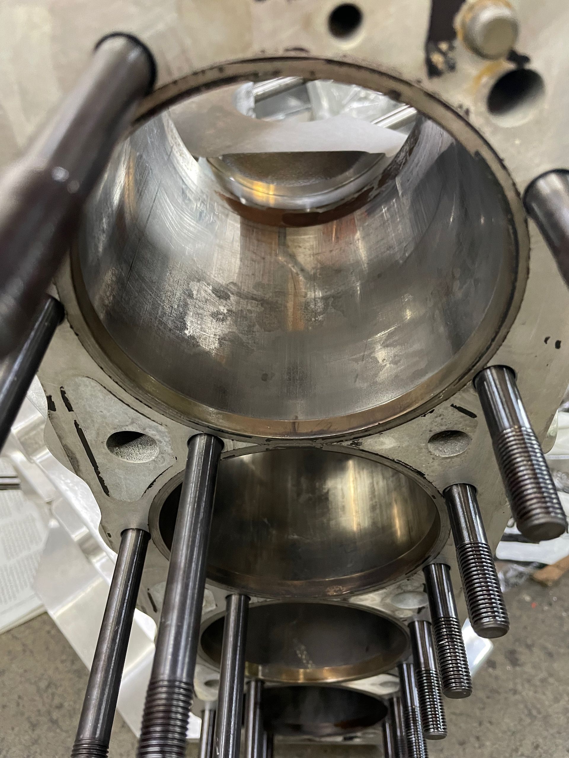 Close-up of a metal engine cylinder bore with pistons and threaded head studs visible