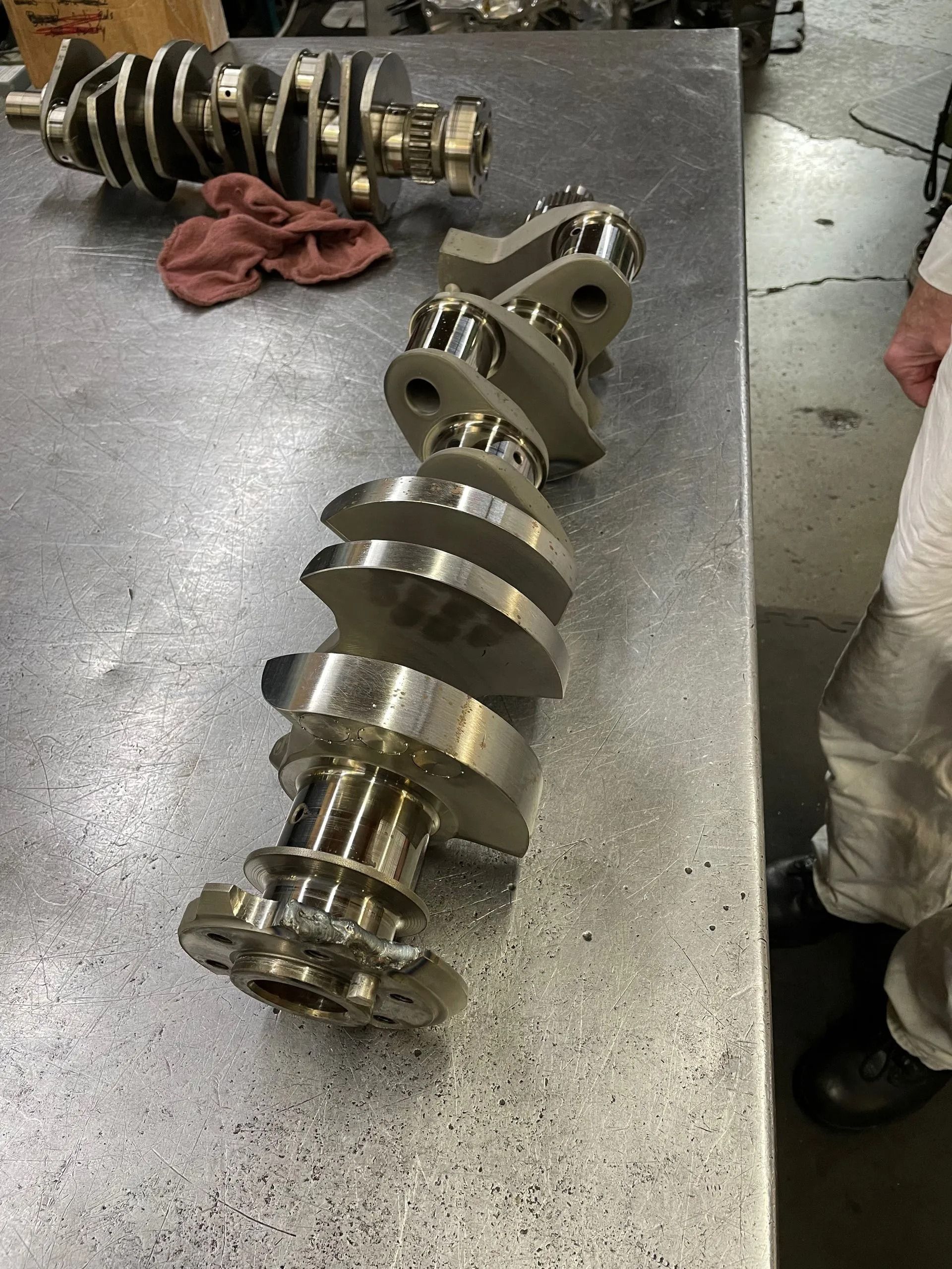 Two large metal crankshafts on a workshop floor, one in the foreground and one behind it.