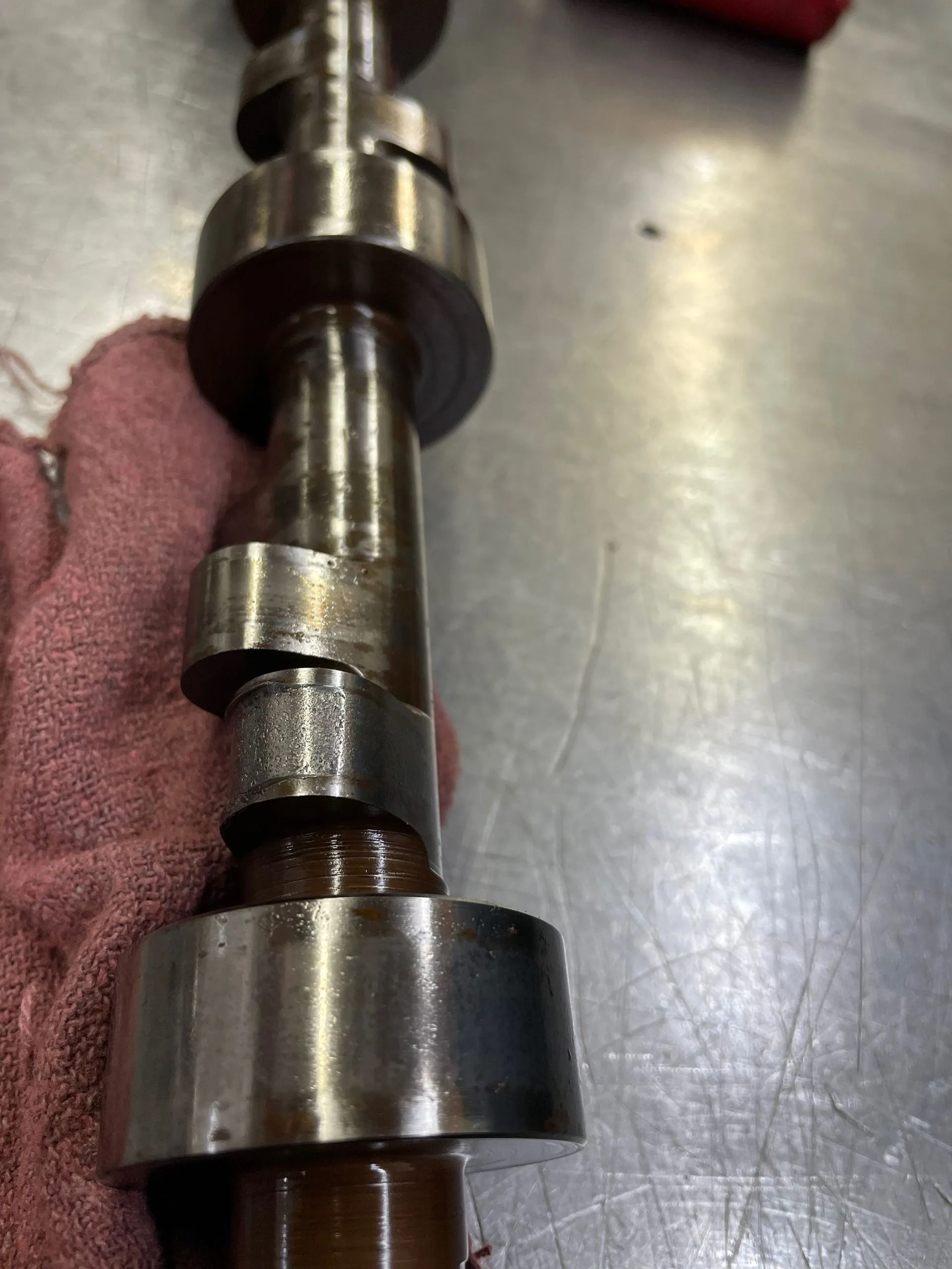 Metal camshaft with several lobes held on a workbench by a gloved hand