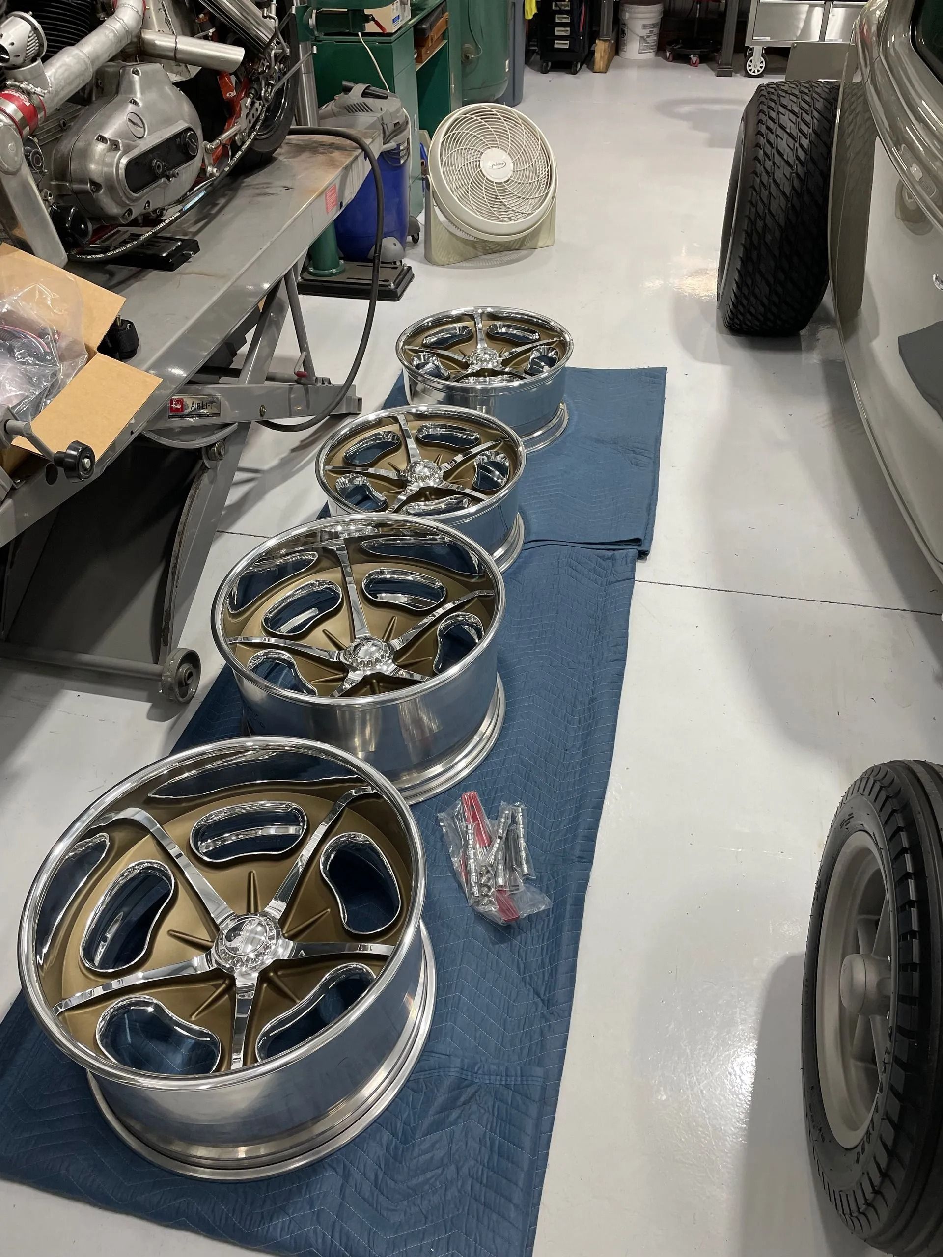 Several car wheels and rims lined up on a blue mat in a garage