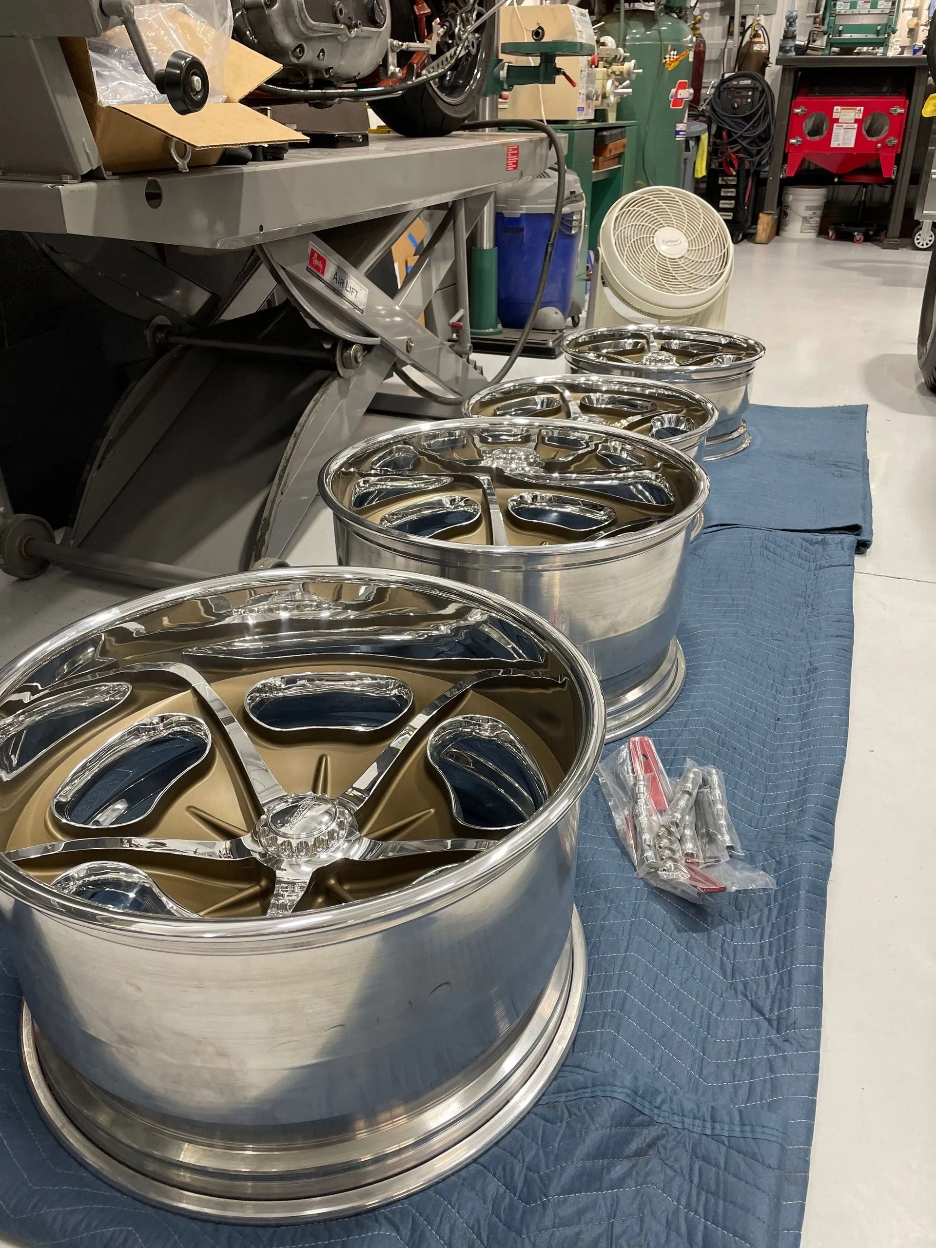 Polished chrome wheels lined up on a blue mat in a garage or workshop