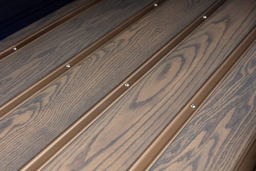 Wood-grain deck boards with narrow metal strips and visible screws arranged diagonally