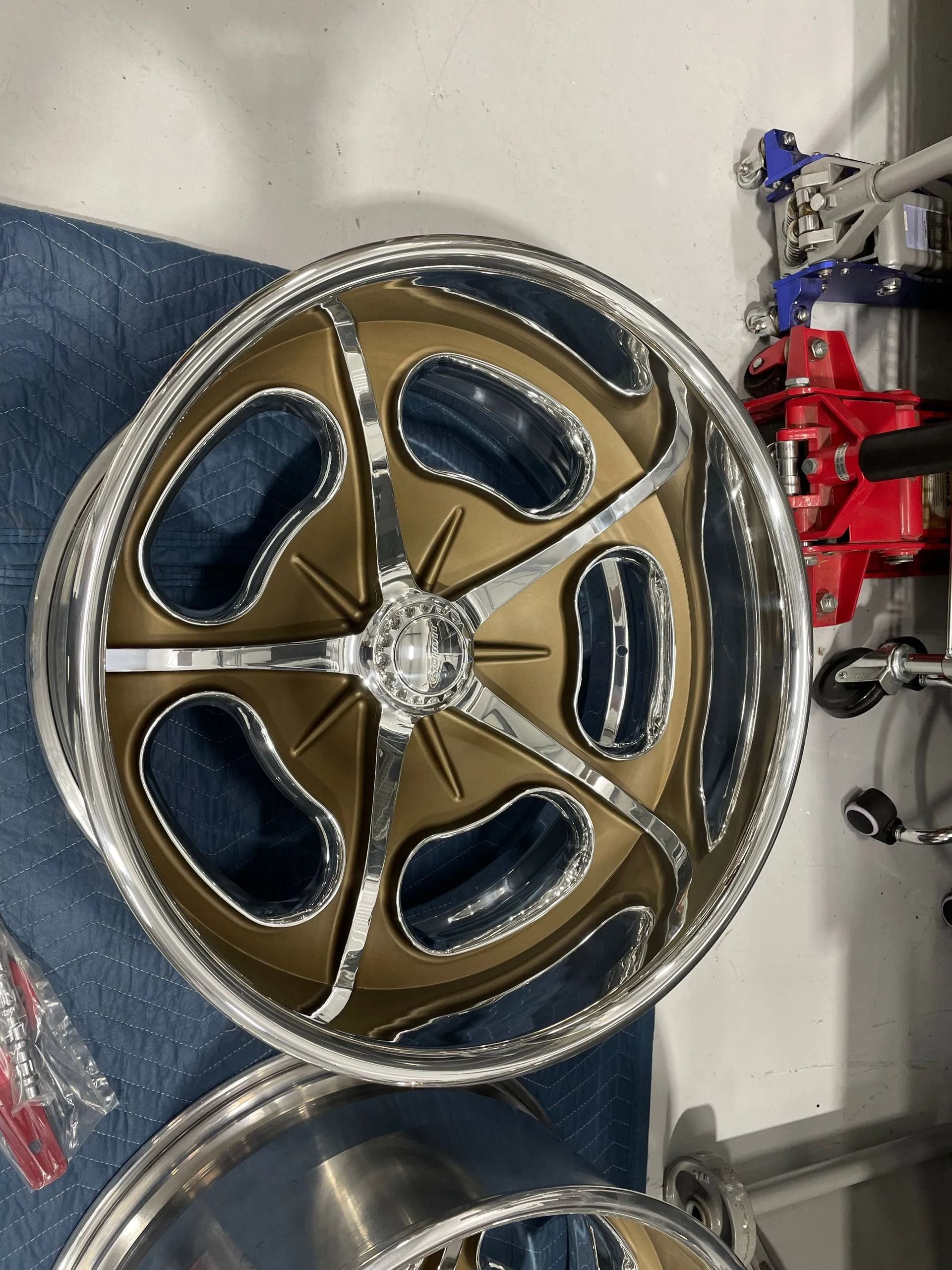 Gold five-spoke car wheel rim on a blue cloth, with red tools and parts in the background