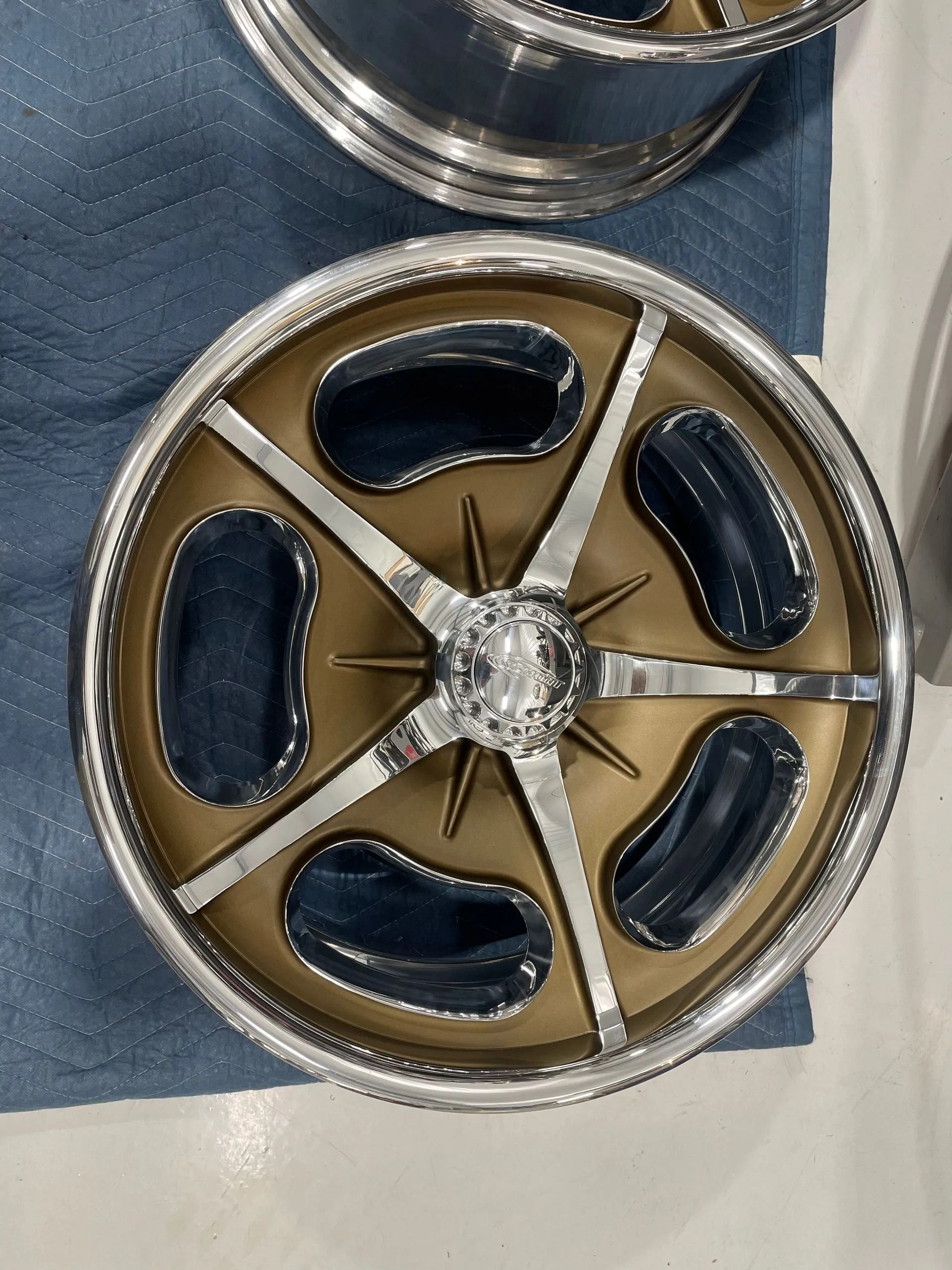 Silver and gold decorative wheel-shaped object with blue insets on a white surface