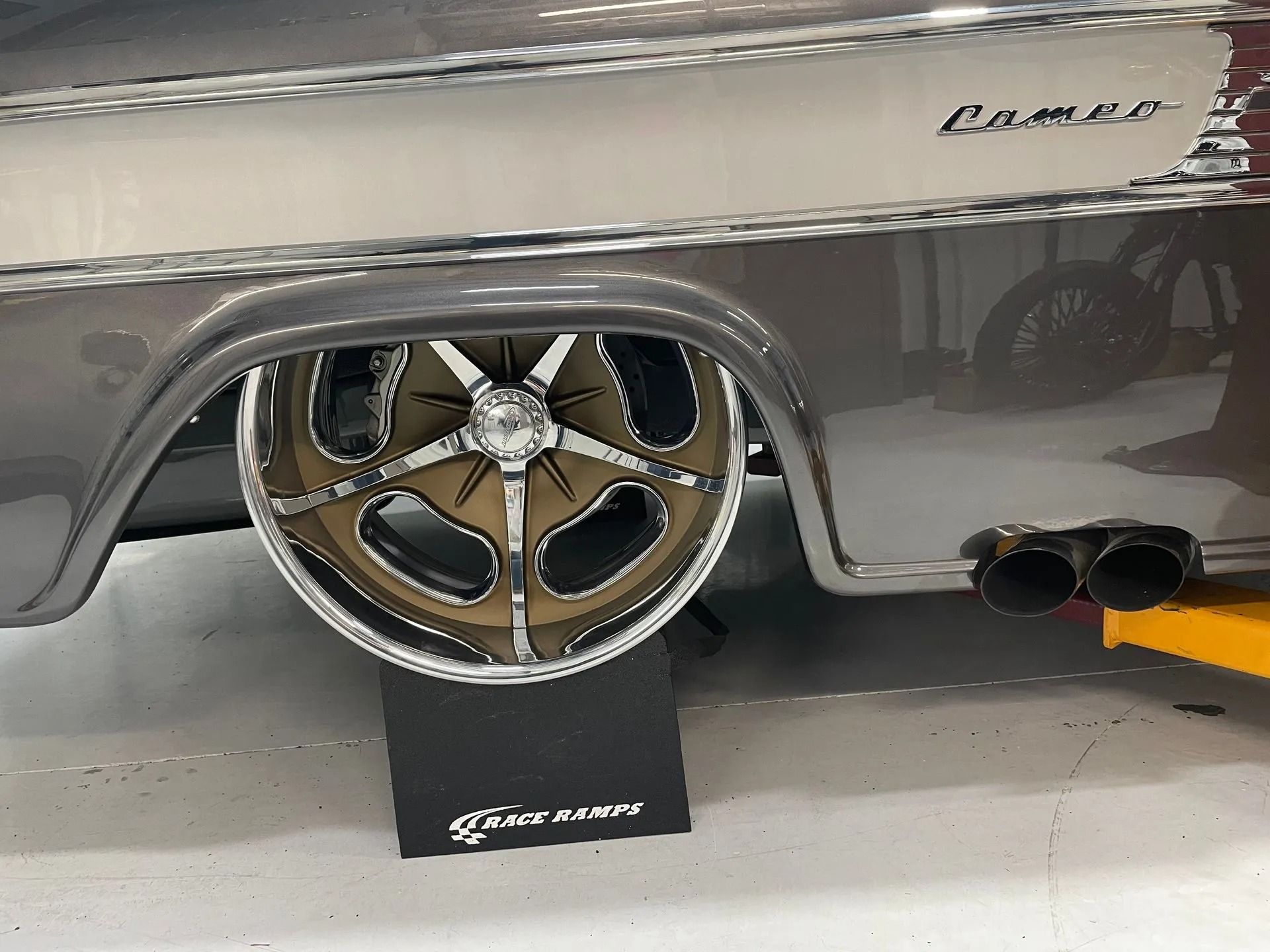 Close-up of a silver Camaro with large chrome wheel on a display stand indoors