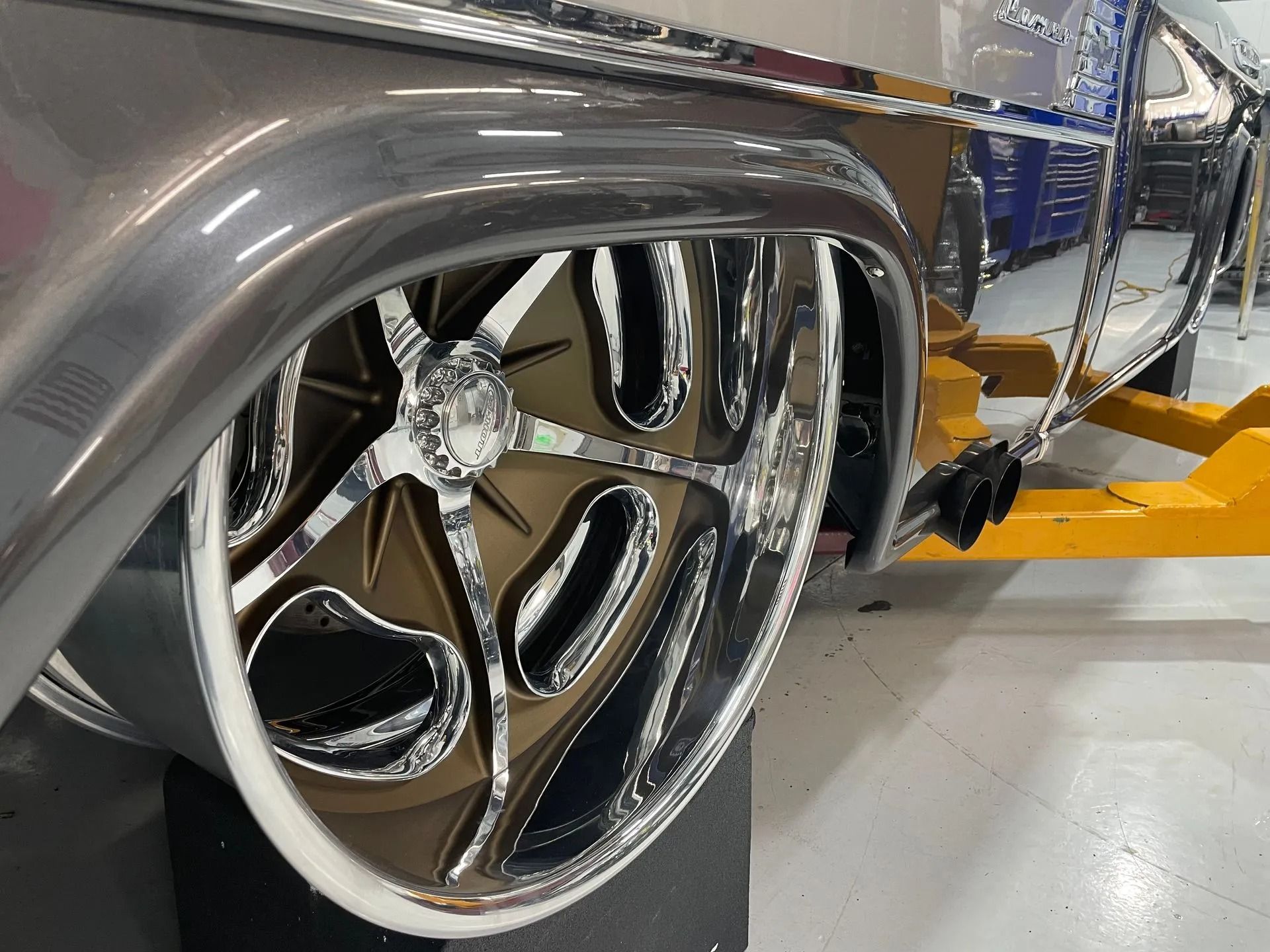 Close-up of a silver car’s chrome wheel and side panel in a garage