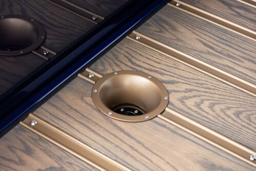 Close-up of a wooden table with built-in brass cup holders and a black divider panel