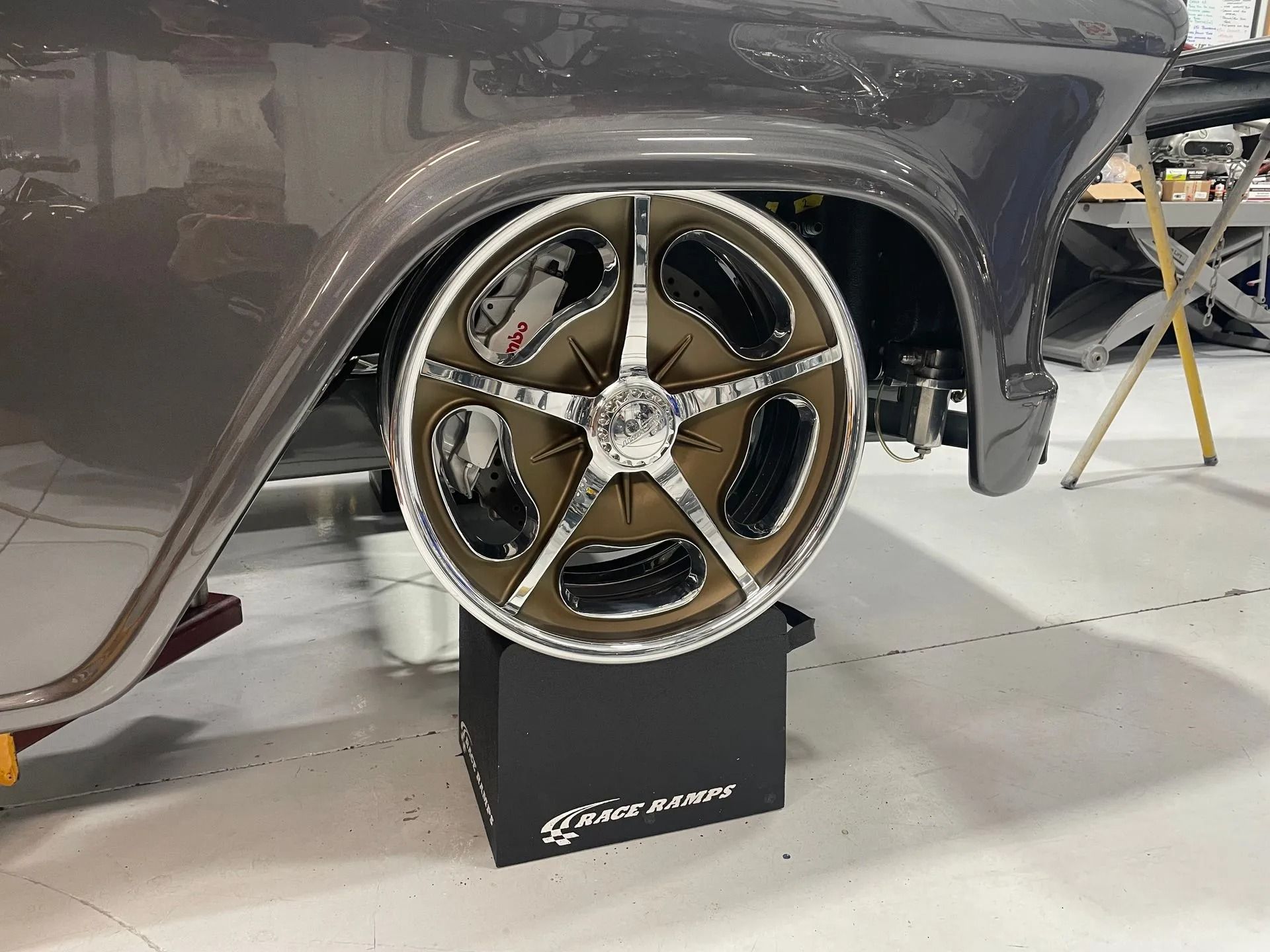 Bronze five-spoke custom wheel mounted on a gray car in a workshop