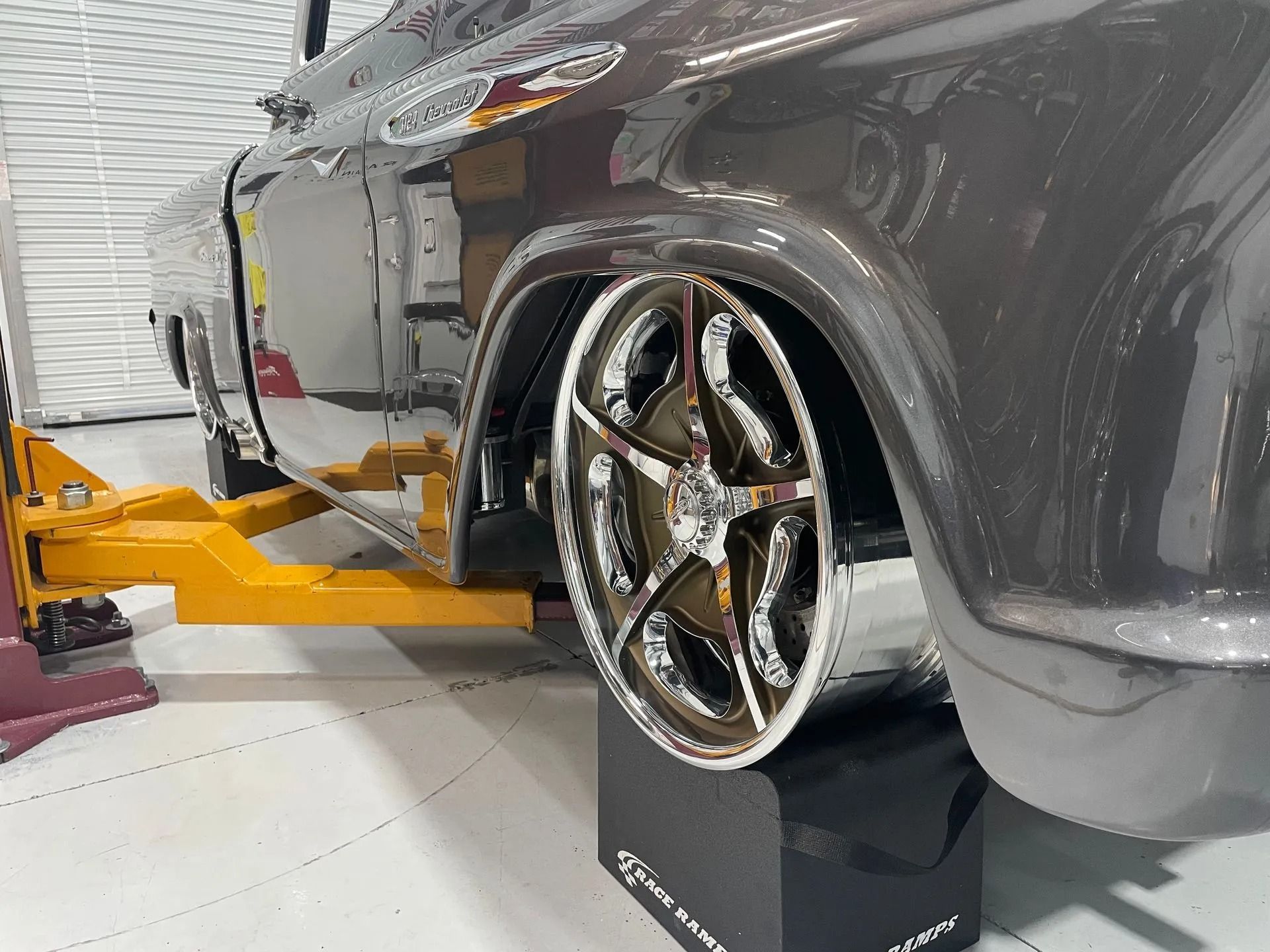 Black classic car on a yellow lift with chrome wheel in an auto shop
