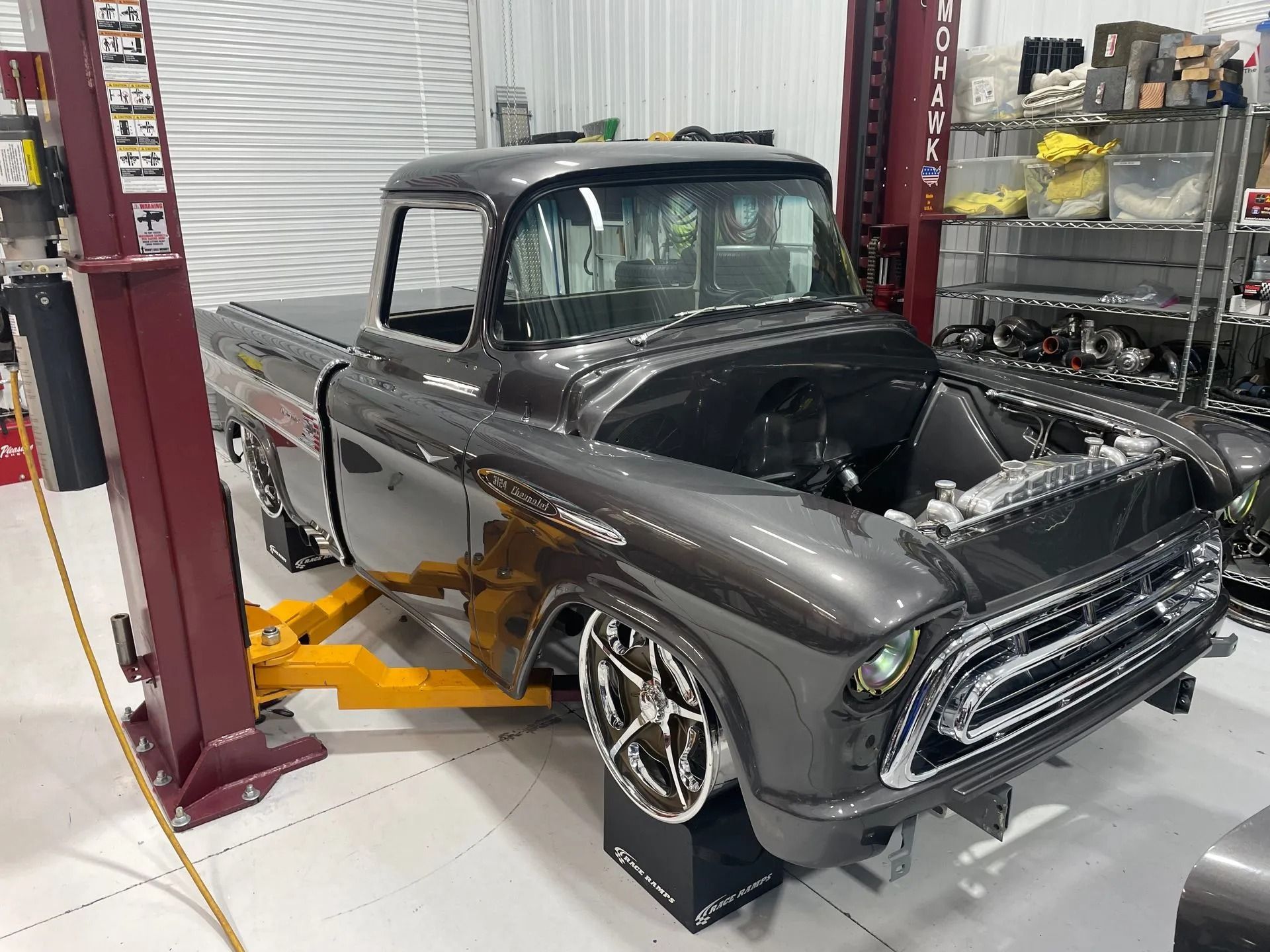Classic black pickup truck on a lift in an auto shop, with polished chrome wheels and front end removed