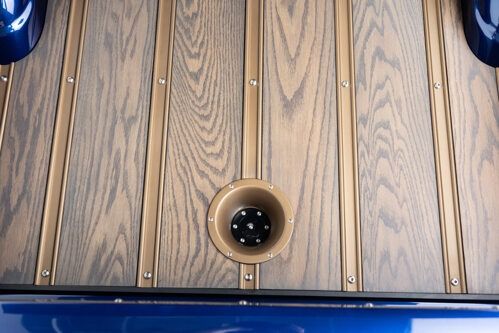 Wood plank deck with a centered brass drain and blue edging on both sides