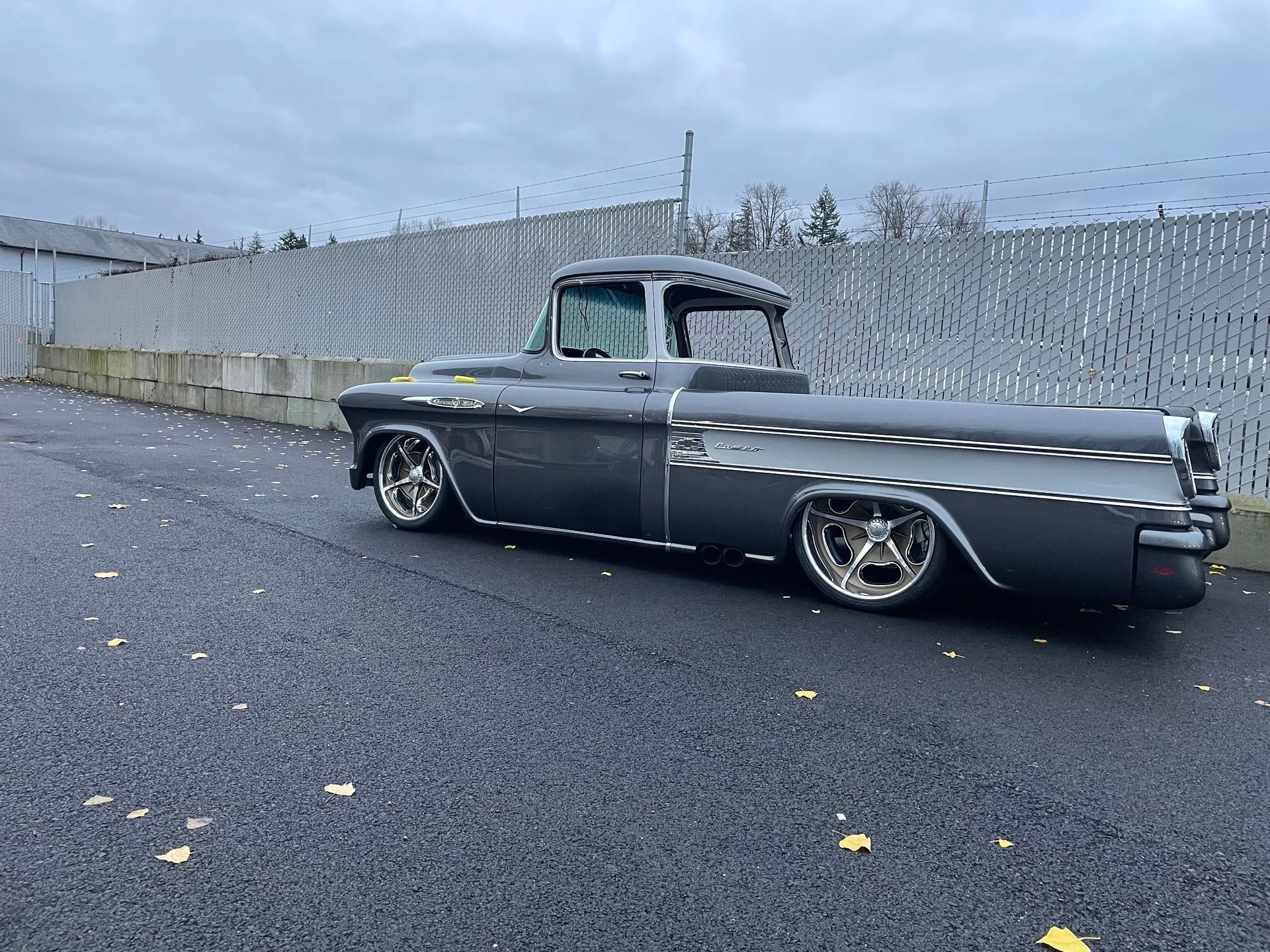 Classic gray pickup truck parked on wet asphalt beside a concrete wall under a cloudy sky