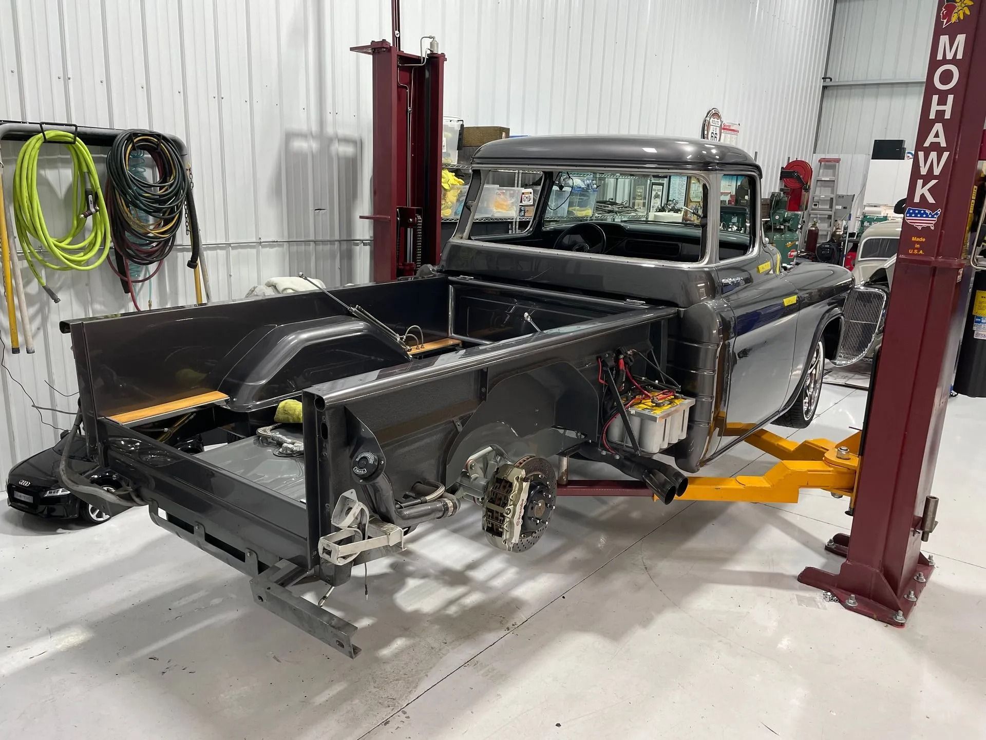 Classic black pickup truck on a lift in a repair shop, with front bodywork removed